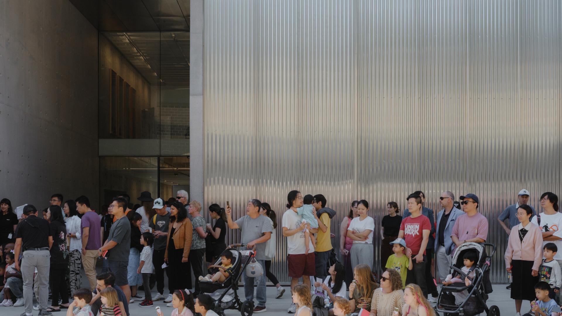 Groups of families, children, parents and prams, sitting outside the new Castle Hill building.