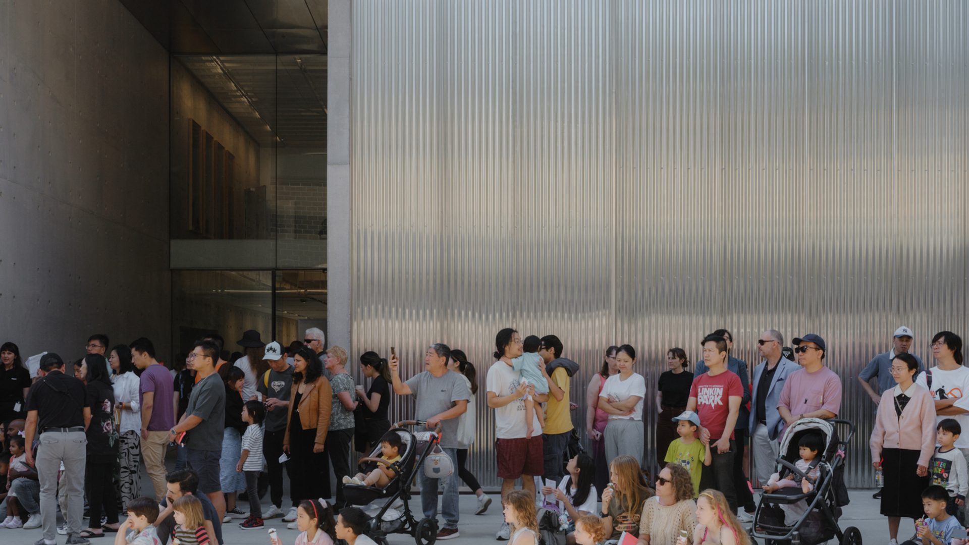 Groups of families, children, parents and prams, sitting outside the new Castle Hill building.