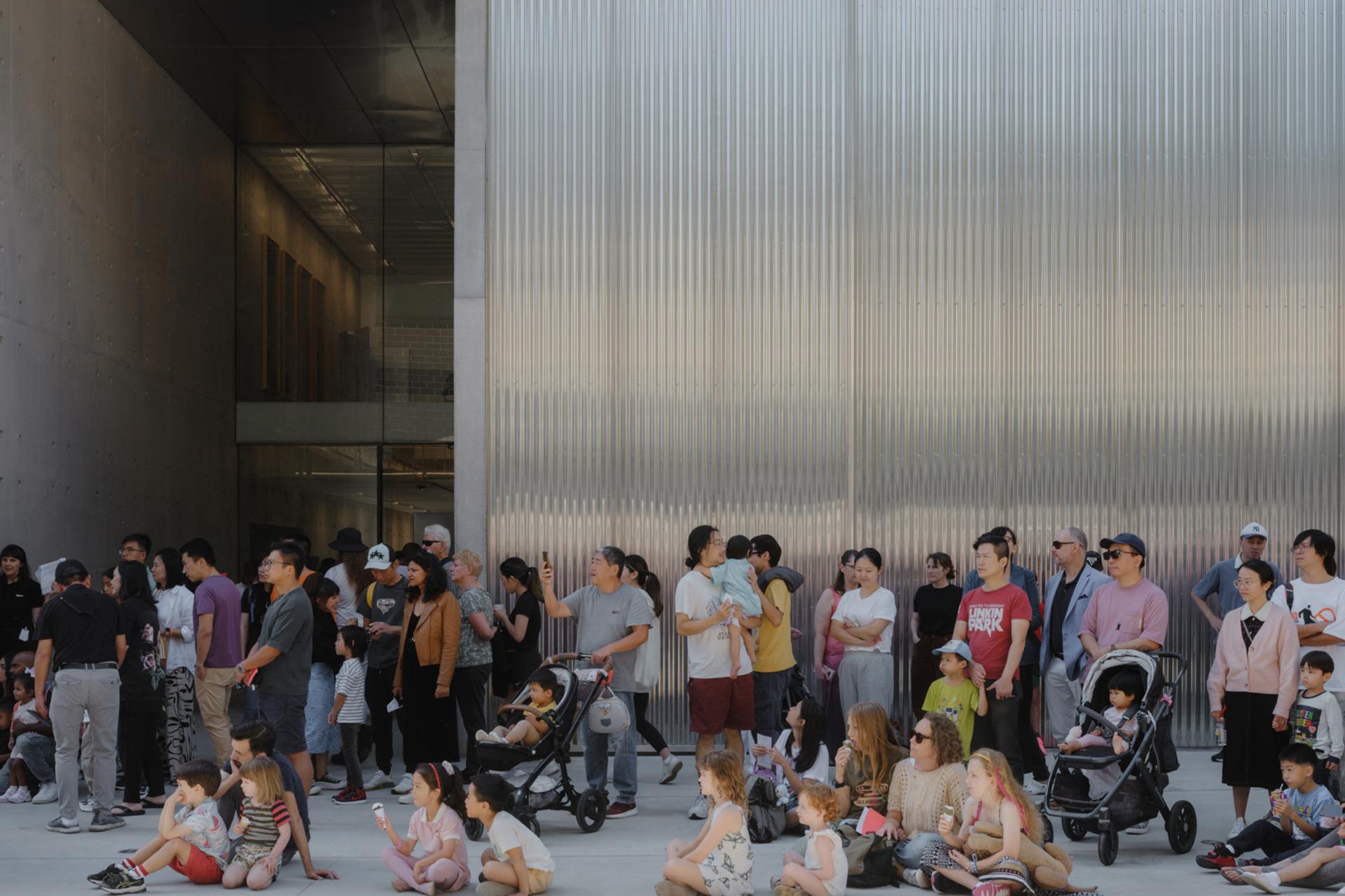Groups of families, children, parents and prams, sitting outside the new Castle Hill building.