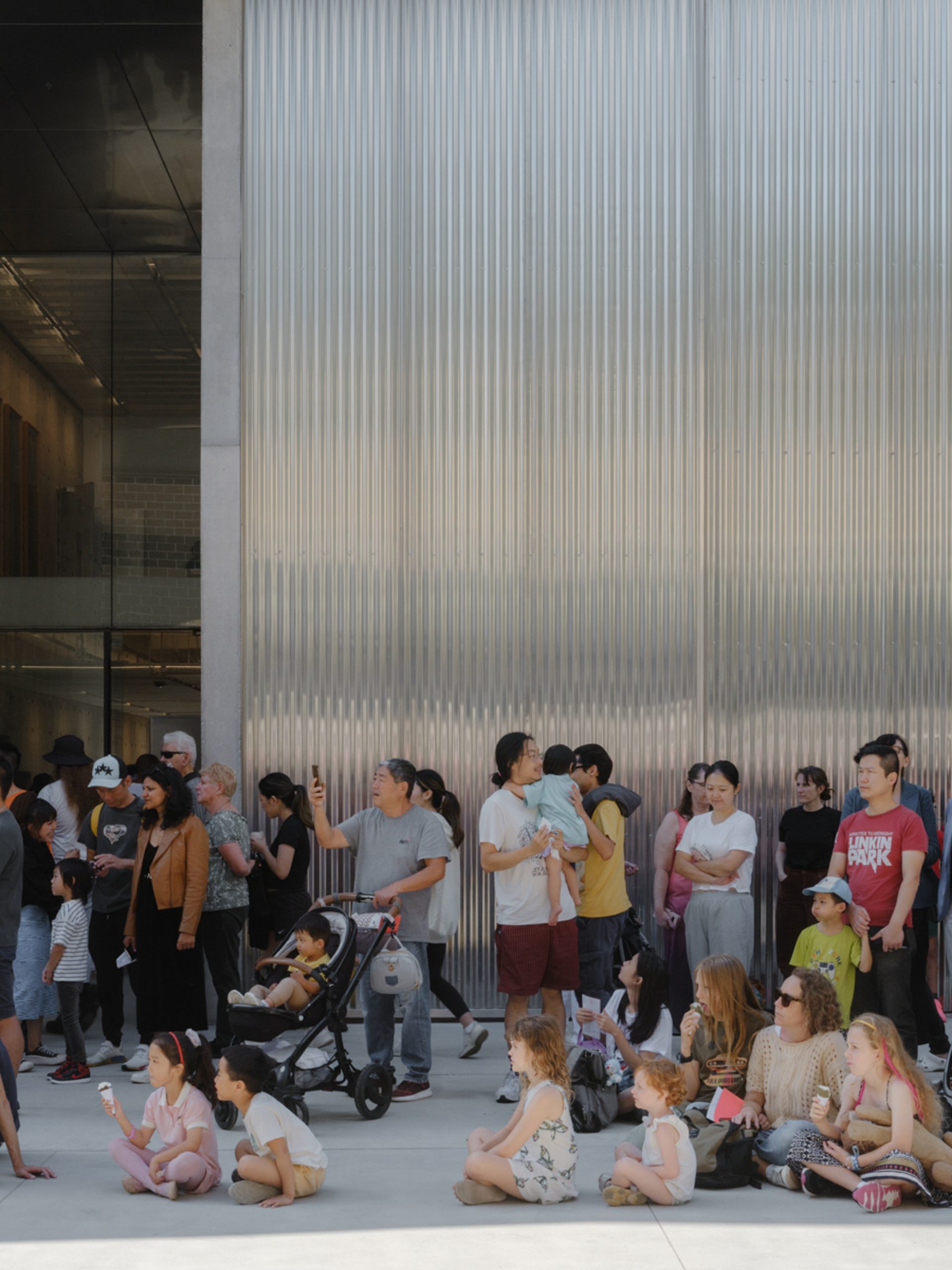Groups of families, children, parents and prams, sitting outside the new Castle Hill building.