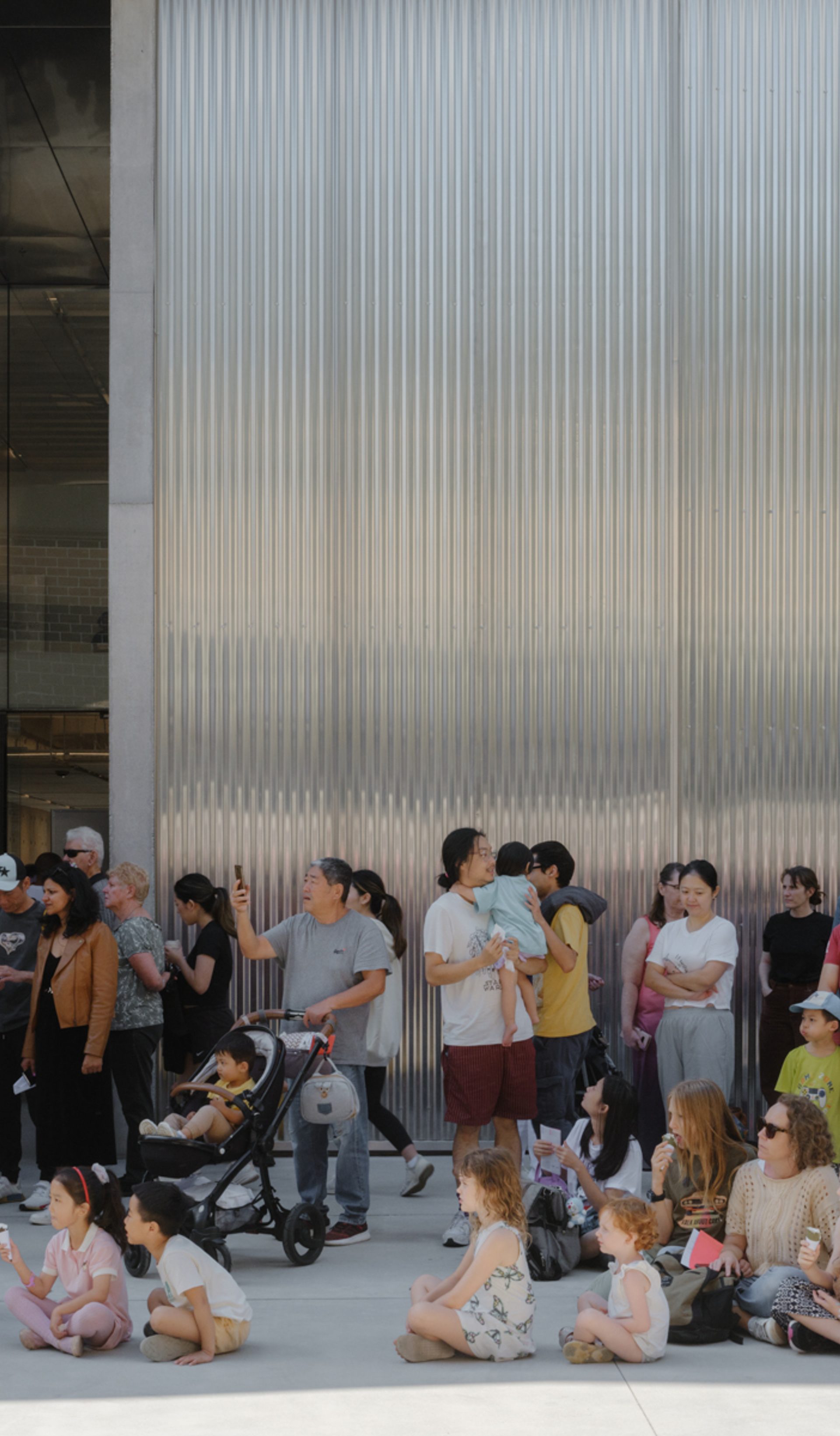 Groups of families, children, parents and prams, sitting outside the new Castle Hill building.