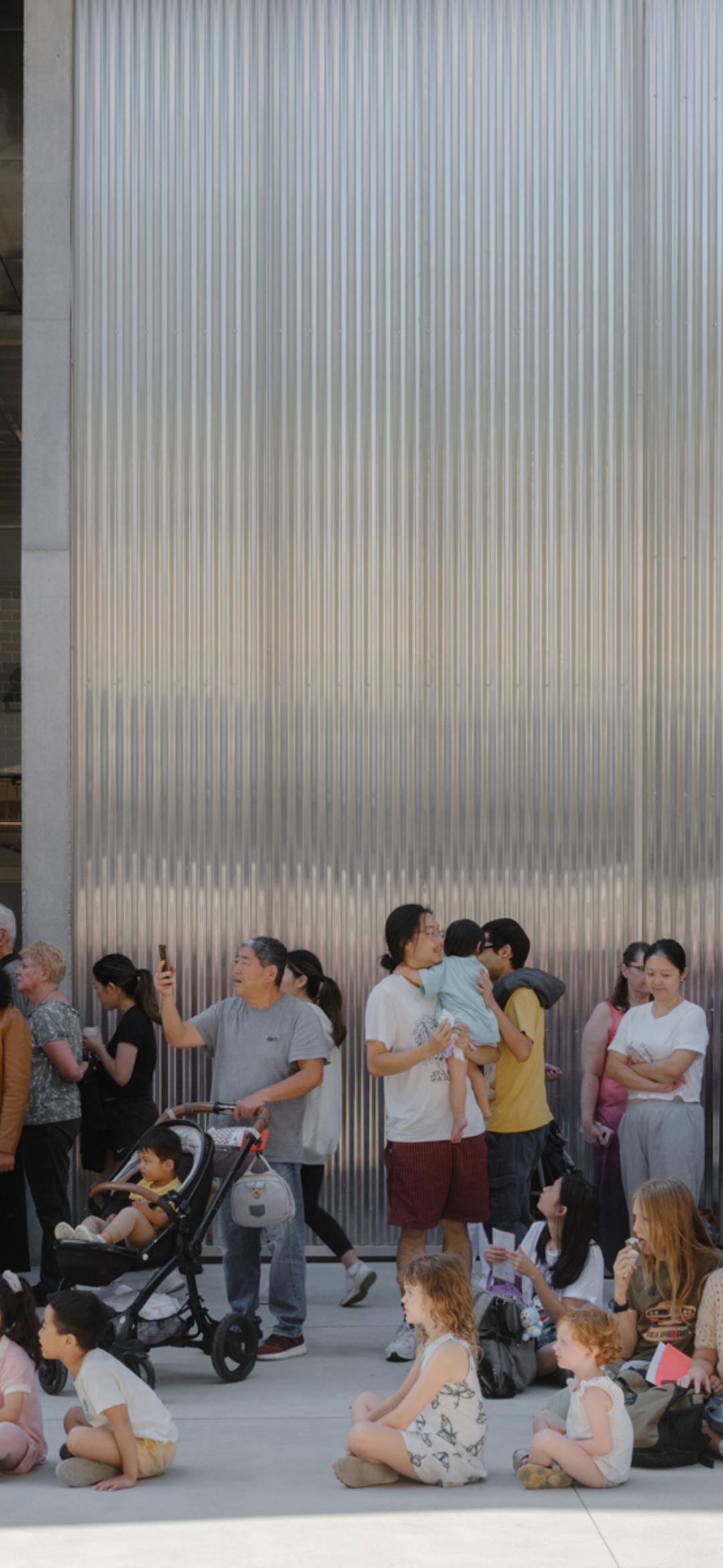 Groups of families, children, parents and prams, sitting outside the new Castle Hill building.