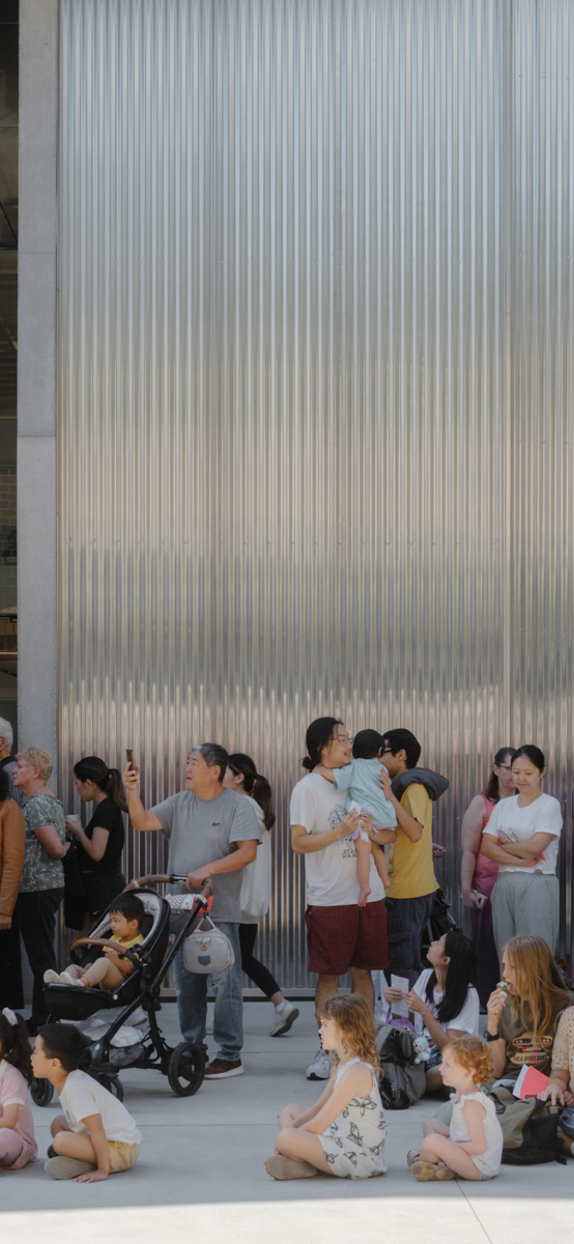 Groups of families, children, parents and prams, sitting outside the new Castle Hill building.