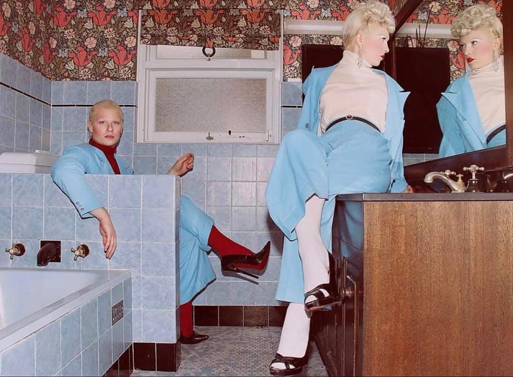 Two people are in a blue tiled bathroom dressed in the same coloured baby blue suit.