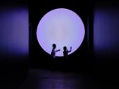 Two young children touch their hands to a big purple circle, that illuminates are dark room.