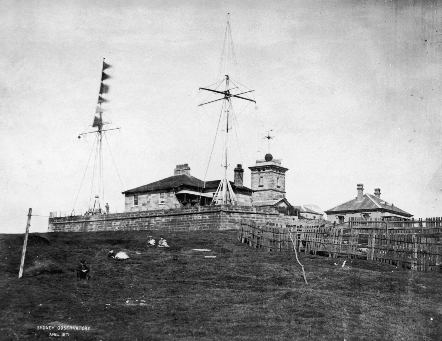 Black and white photograph of flagstaff perched on a hill, with a building behind