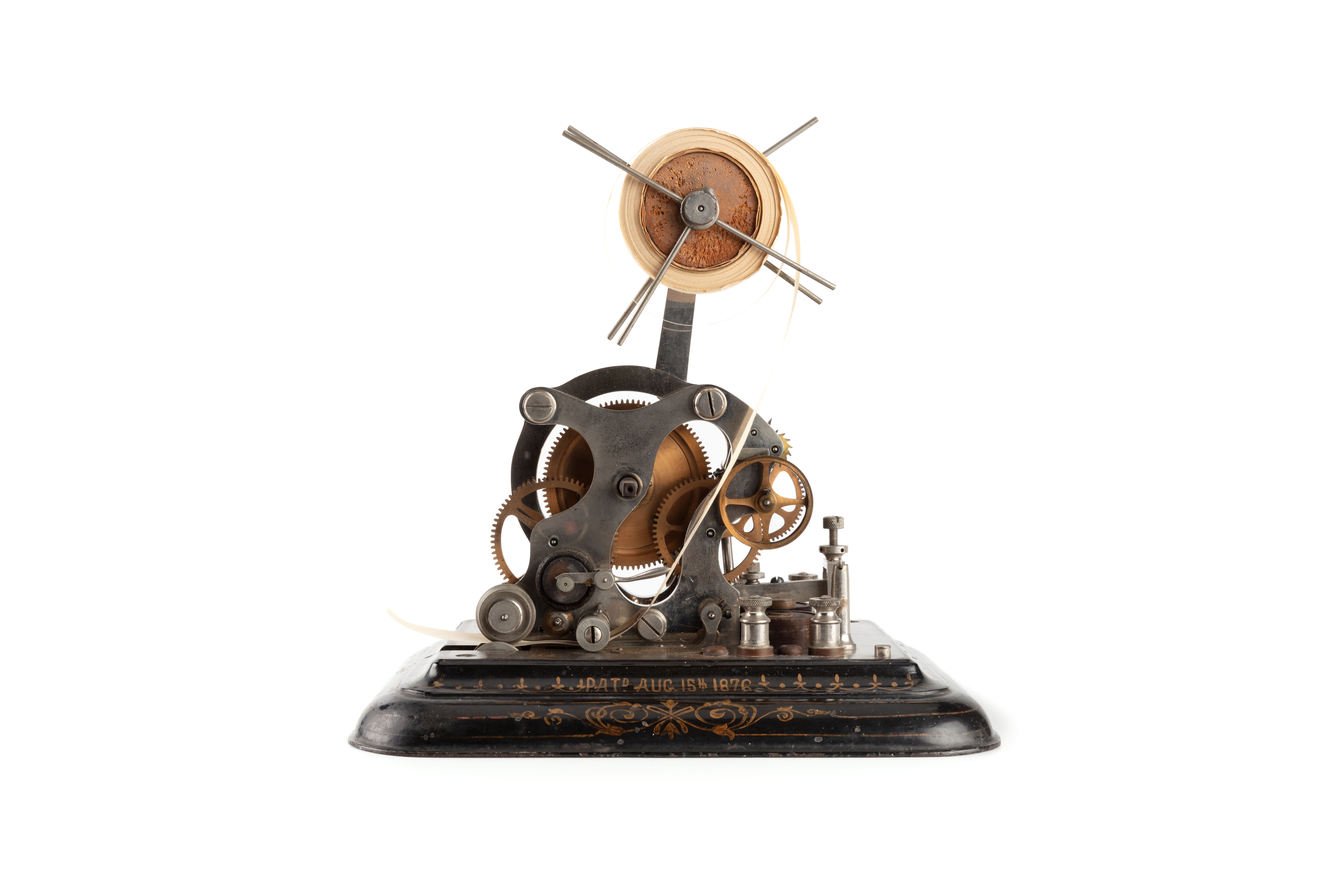 Photograph of a machine made of intricate metal cogs and mechanics, a morse code ink writer. A roll of paper is held at the top of the machine, used to print the morse code onto.
