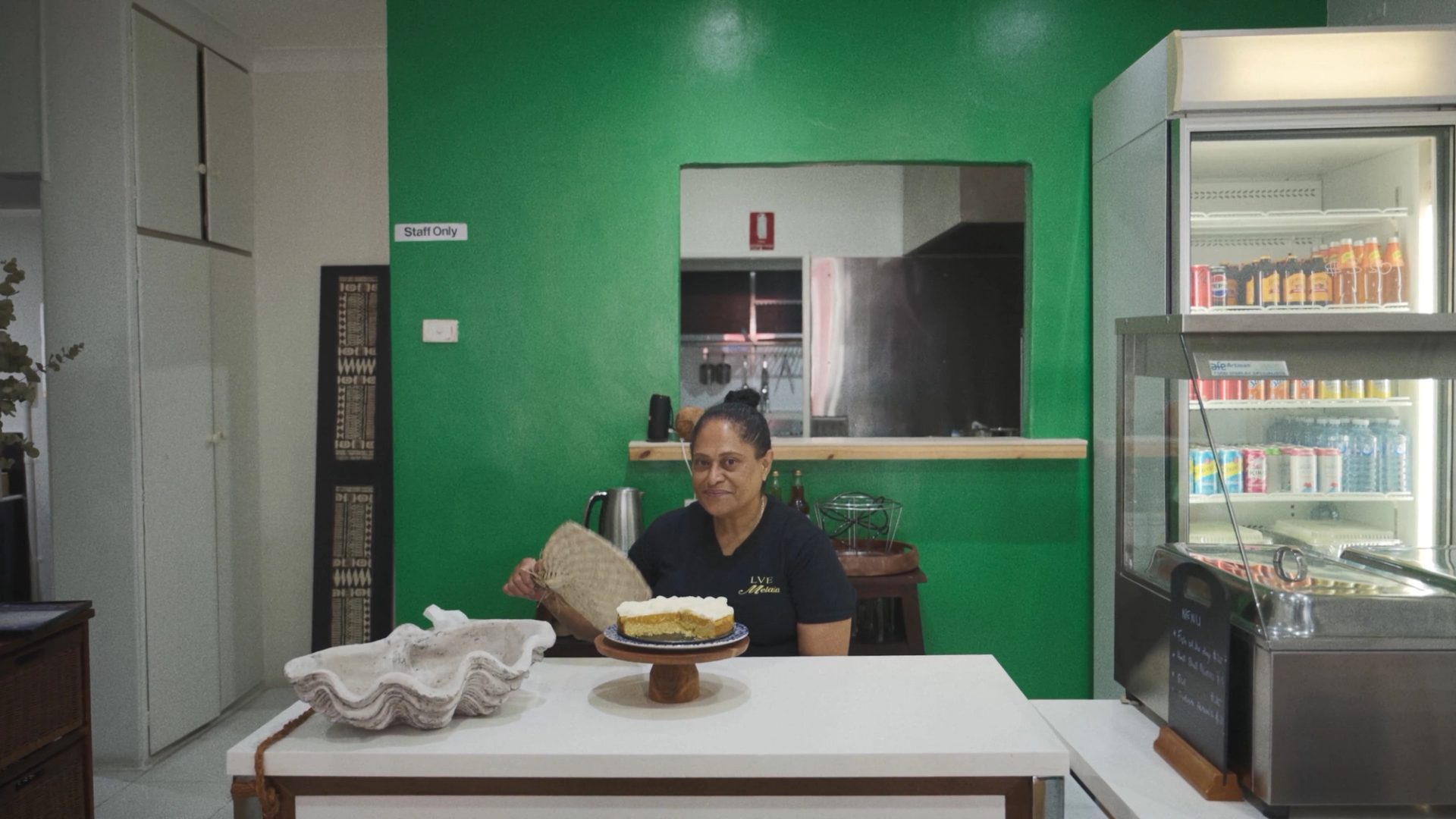 A woman sitting with an iri (Fijian fan), with a cake in front of her.