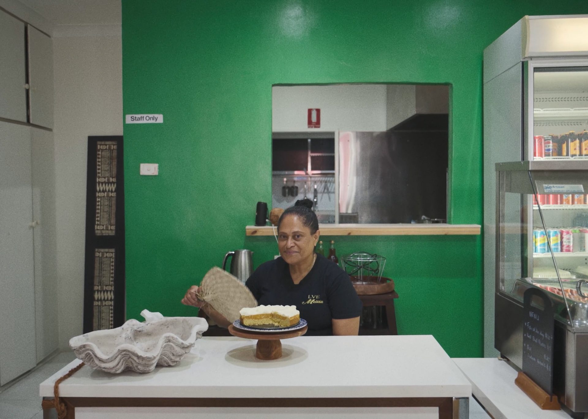 A woman sitting with an iri (Fijian fan), with a cake in front of her.