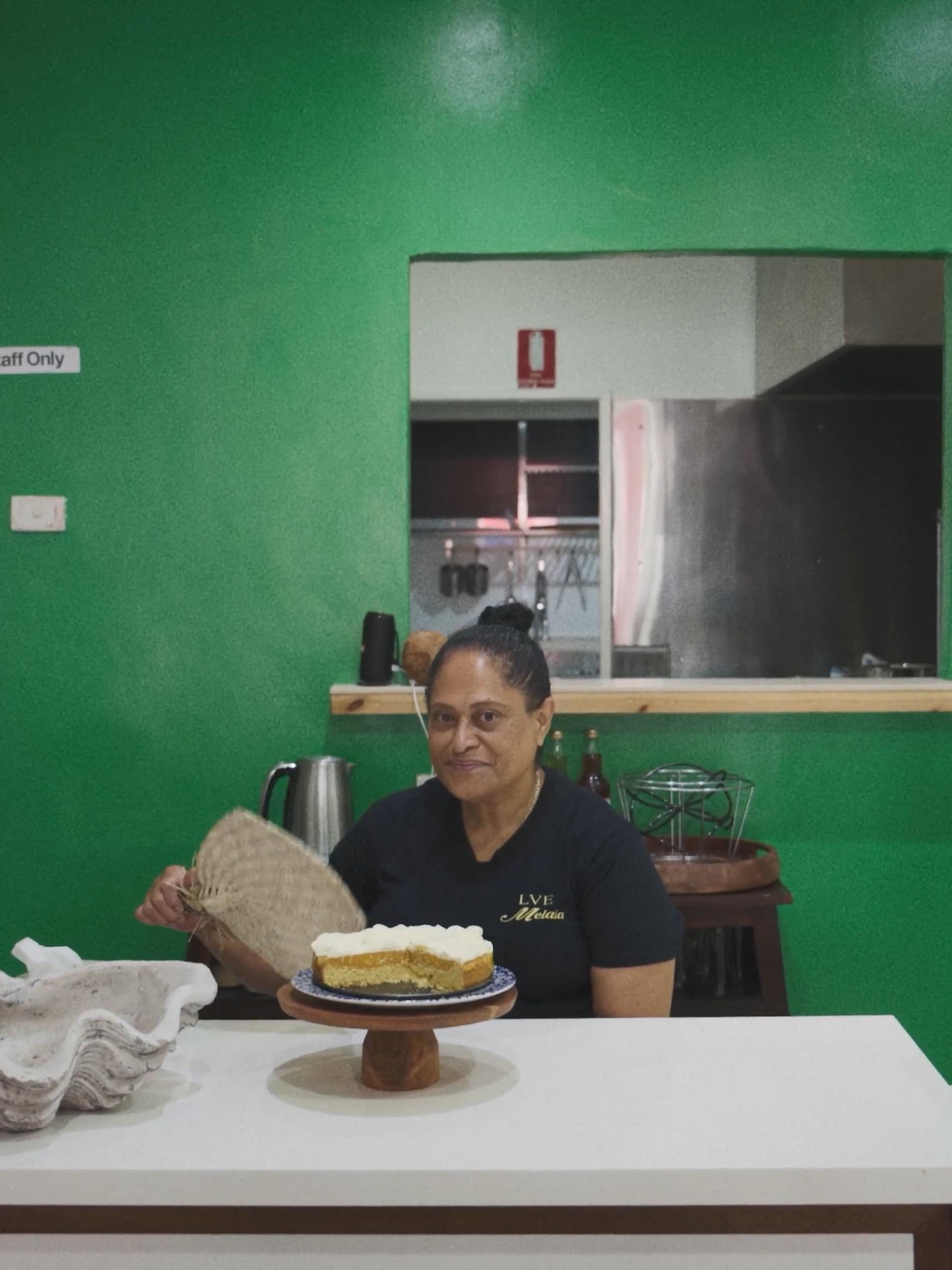 A woman sitting with an iri (Fijian fan), with a cake in front of her.