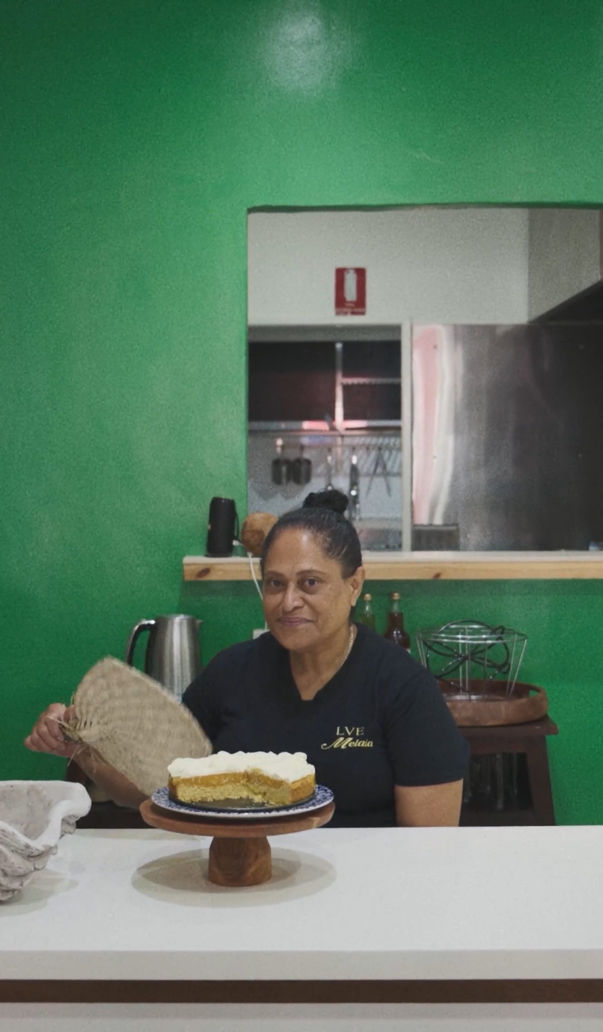 A woman sitting with an iri (Fijian fan), with a cake in front of her.