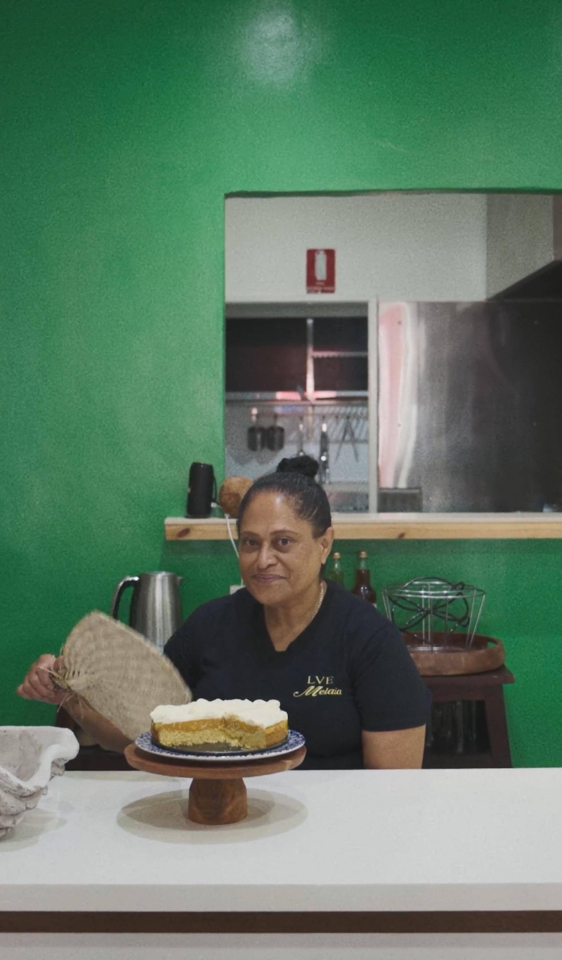 A woman sitting with an iri (Fijian fan), with a cake in front of her.