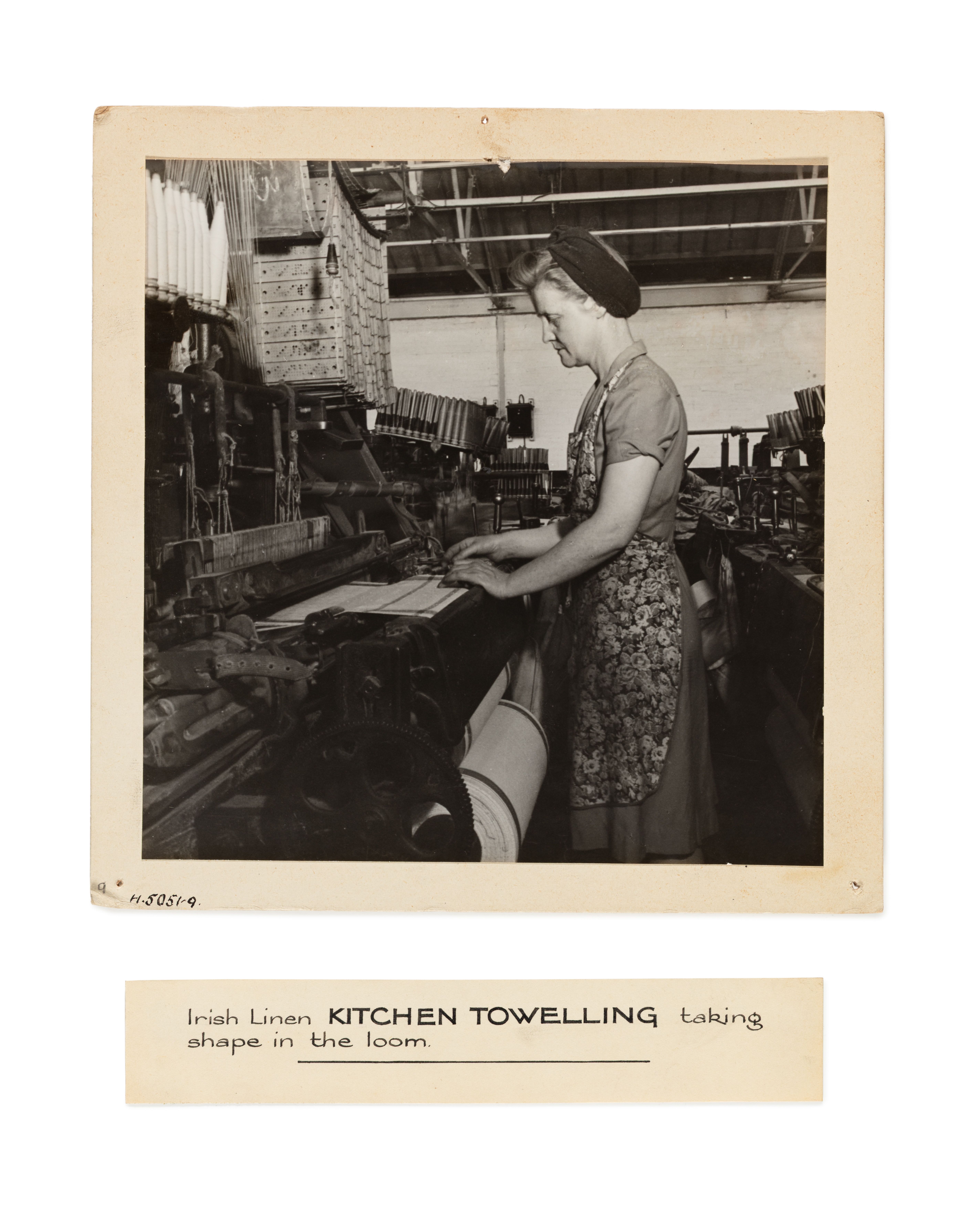 A photograph depicting 'Irish Linen kitchen towelling taking shape in the loom'. There is an associated and detatched label.