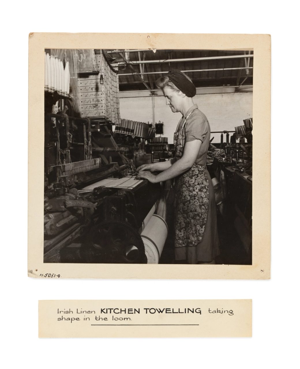 A photograph depicting 'Irish Linen kitchen towelling taking shape in the loom'. There is an associated and detatched label.