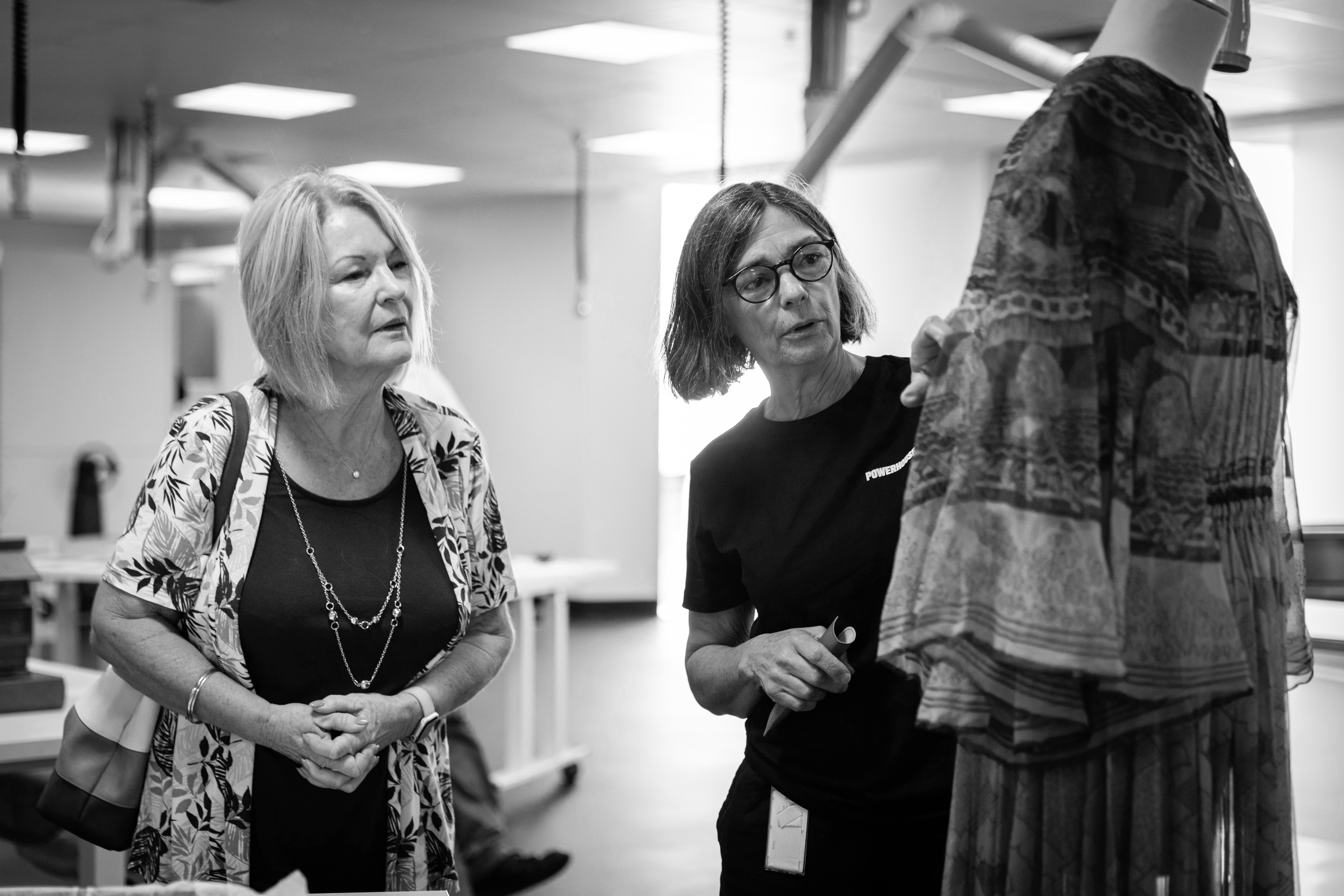 Black and white photo of two women looking at a mannequin wearing a loose dress.