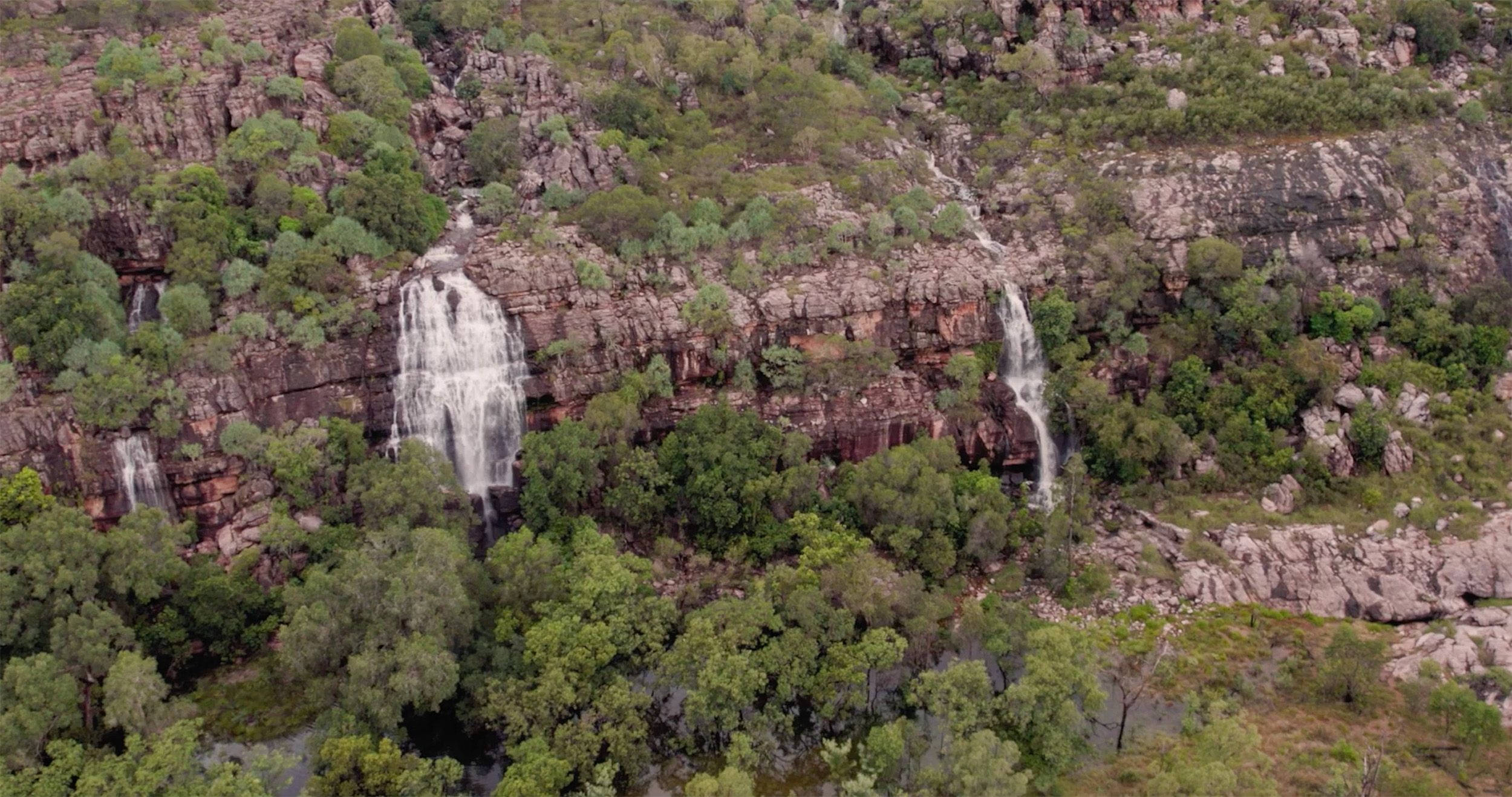 A wide shot of a green, cliff side landscape. There are several waterfalls running down the side of the cliffs.