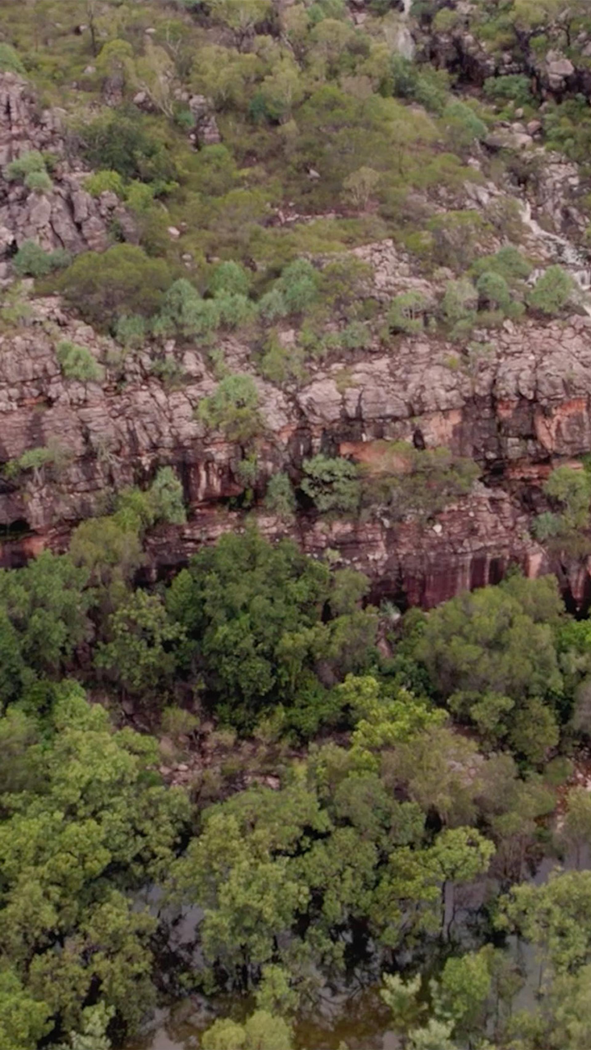A wide shot of a green, cliff side landscape. There are several waterfalls running down the side of the cliffs.