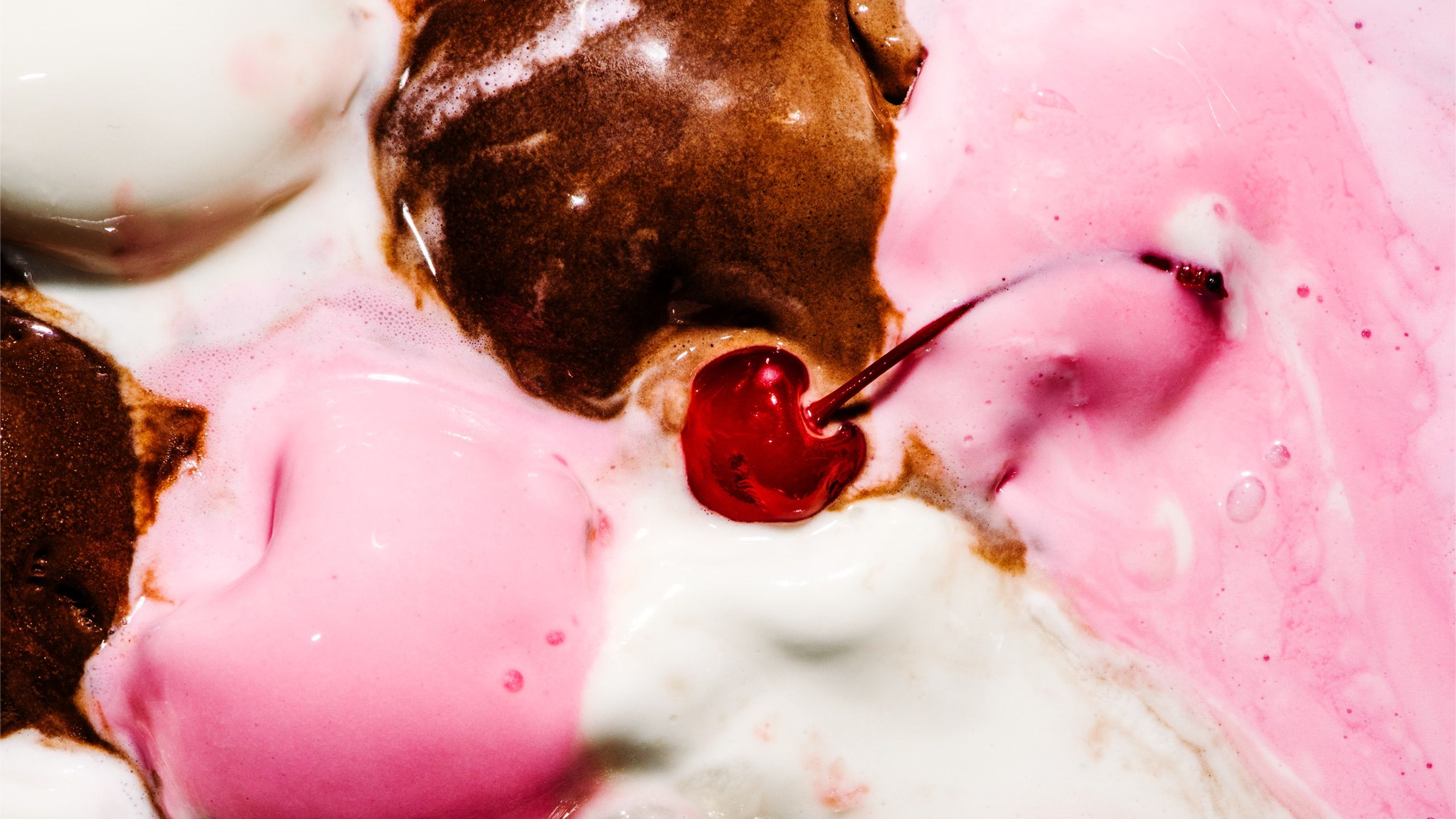 A close up of melted Neapolitan ice cream with a glace cherry in the centre.