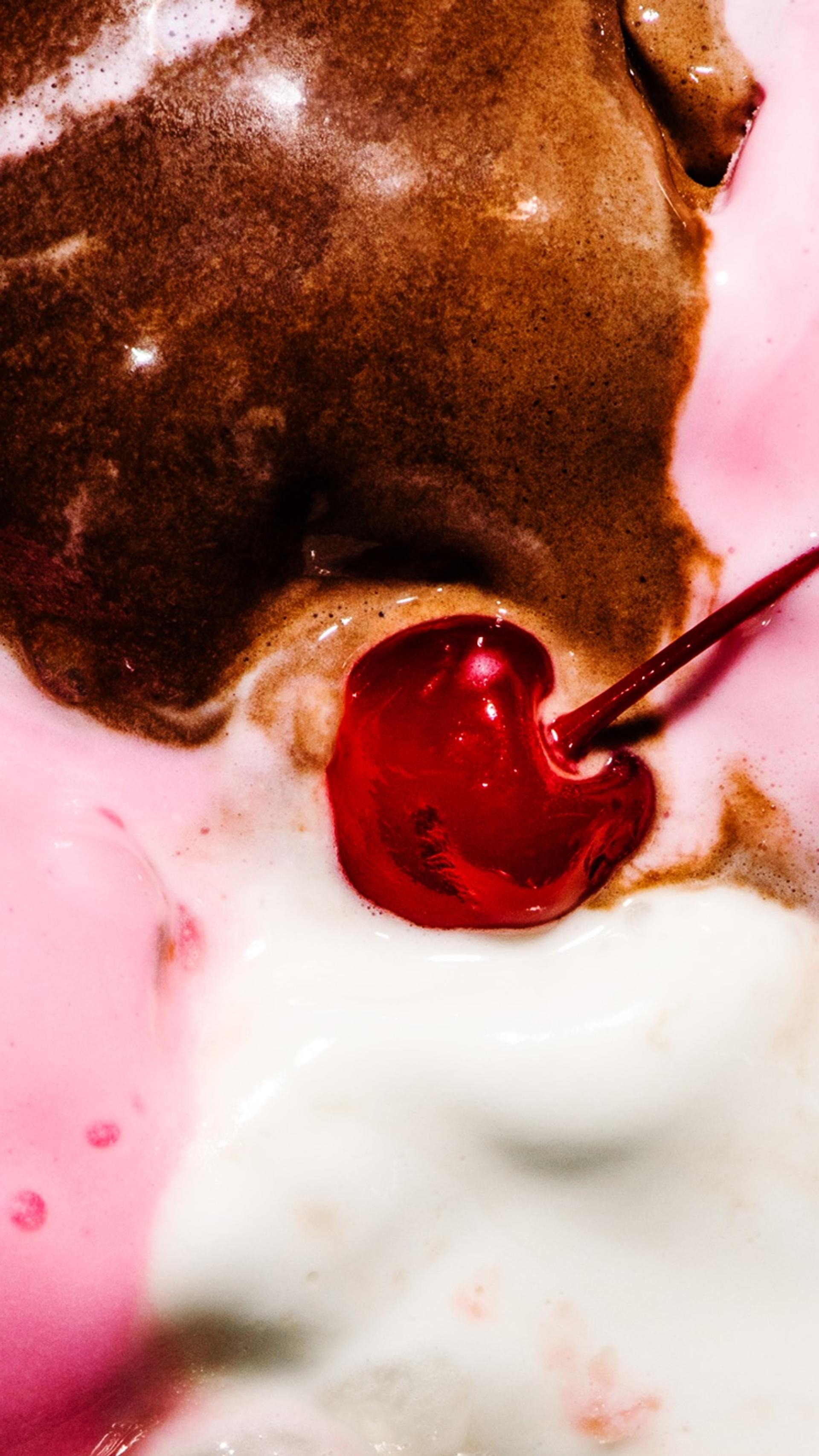 A close up of melted Neapolitan ice cream with a glace cherry in the centre.