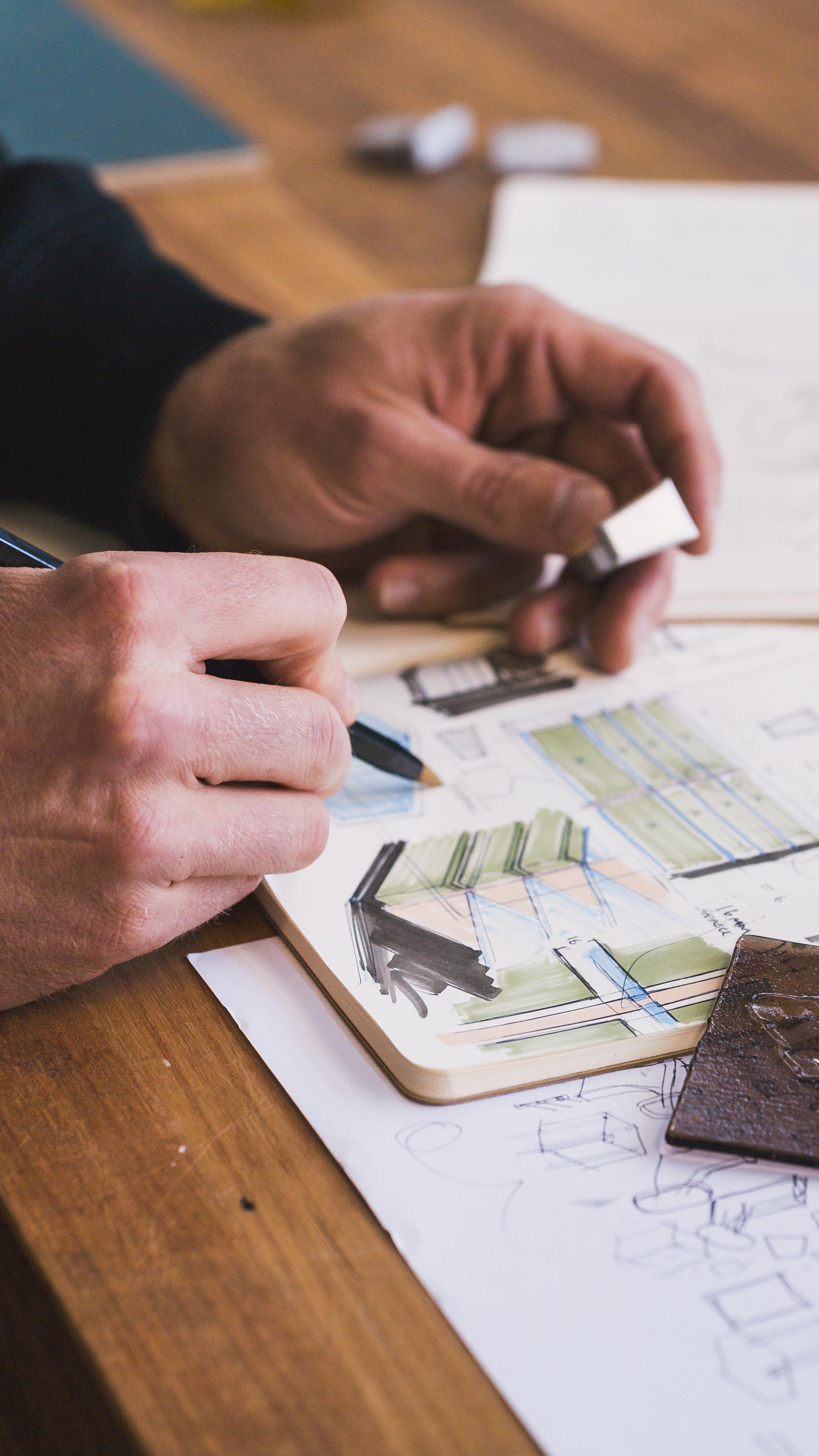 A man adds to a notebook of hand drawn design sketches.