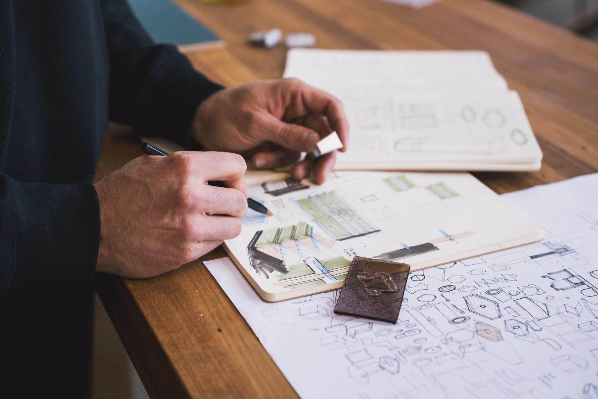 A man adds to a notebook of hand drawn design sketches.
