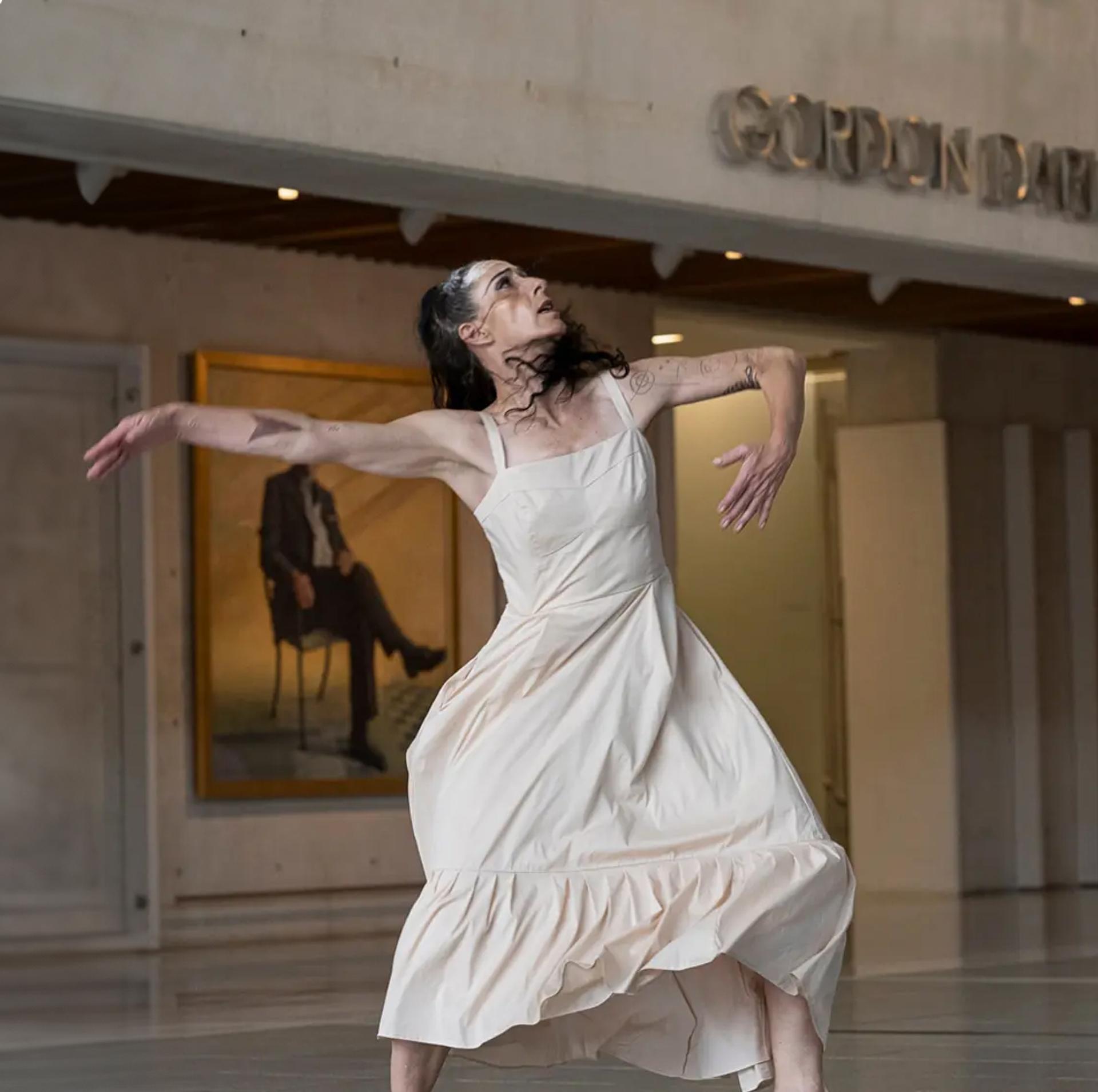 Woman dancing wearing long cream-coloured dress.