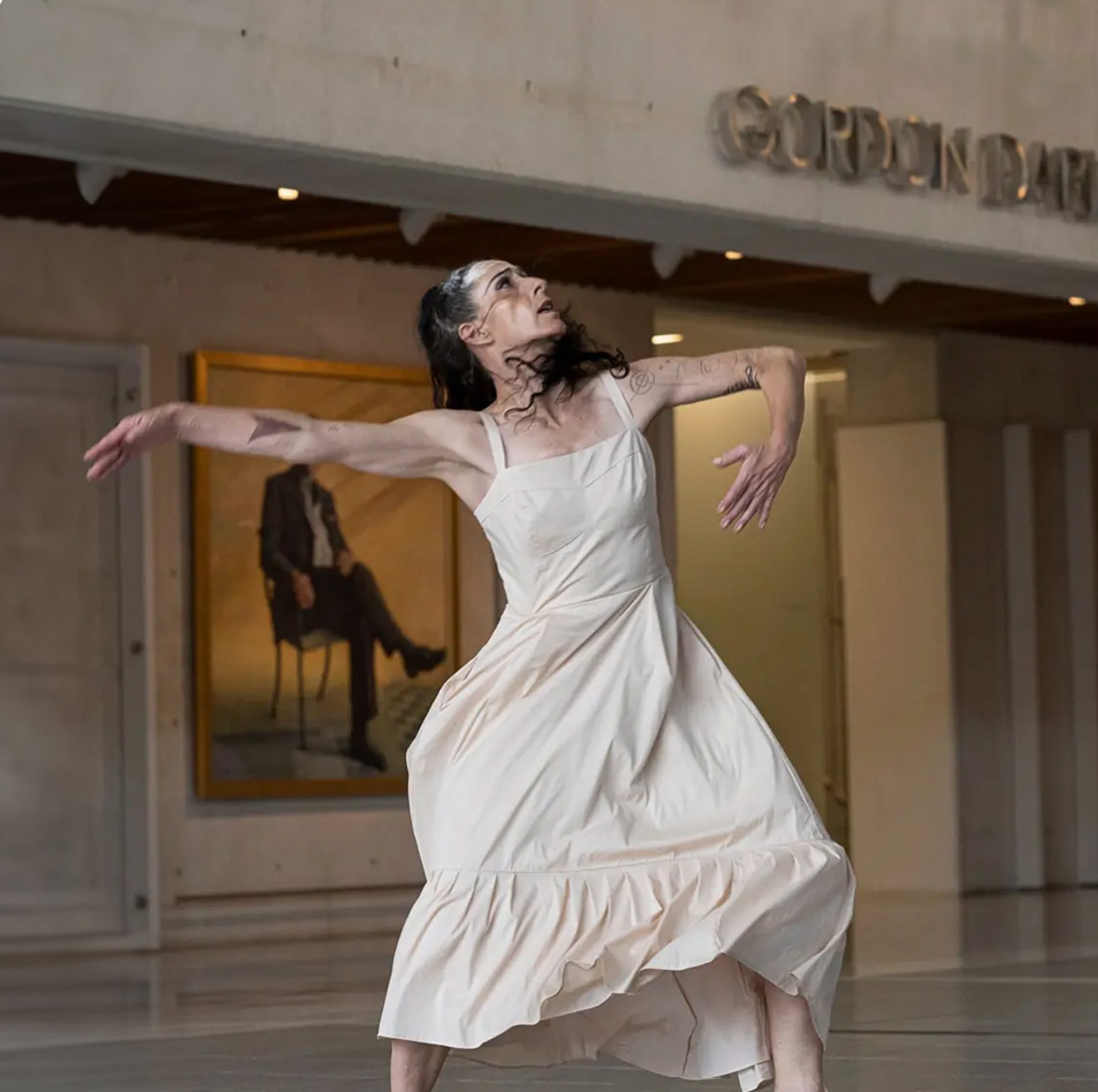 Woman dancing wearing long cream-coloured dress.