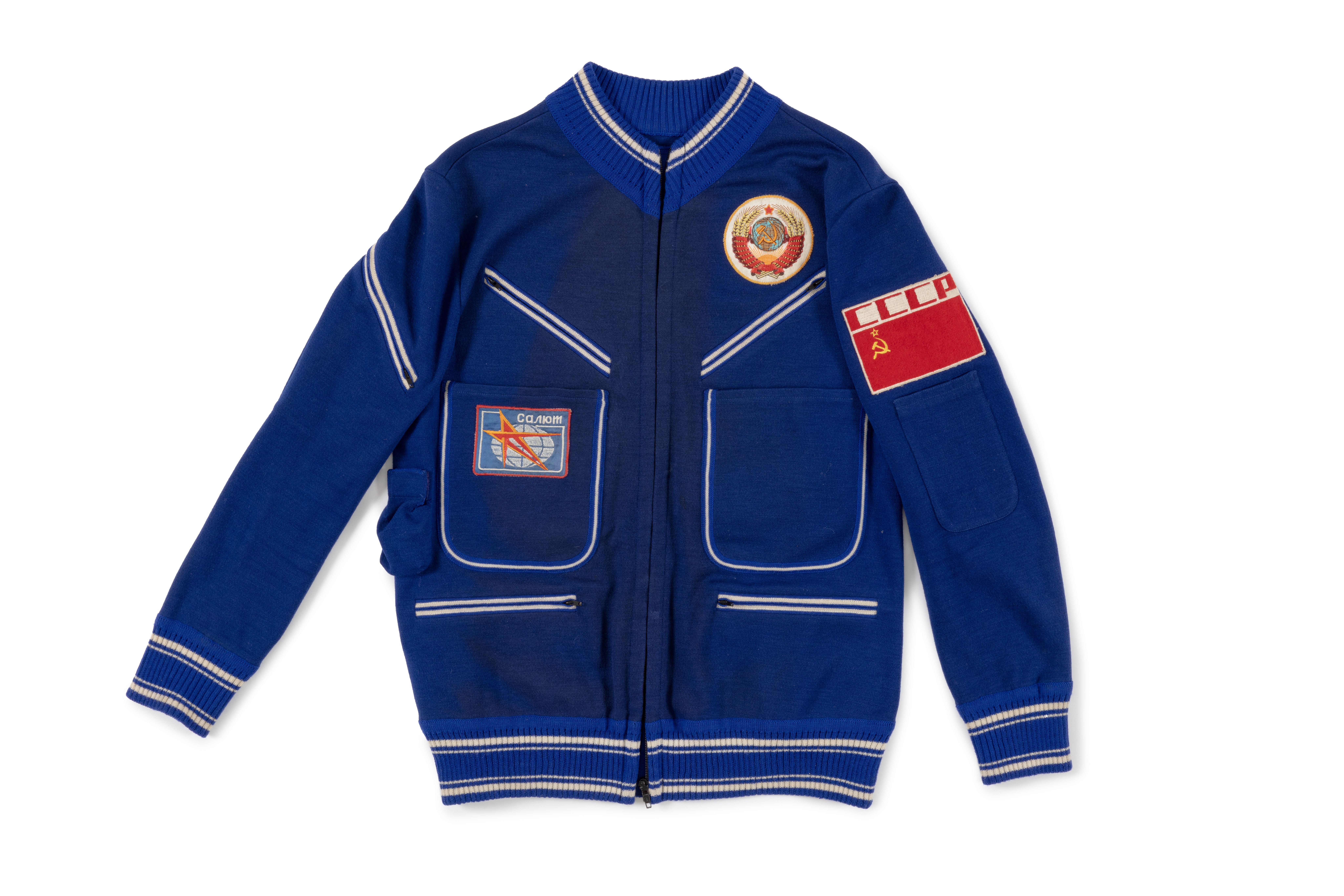 Photograph of the light jacket a part of a five piece royal blue polyester wool blend flight suit with white trims, emblems and patches.