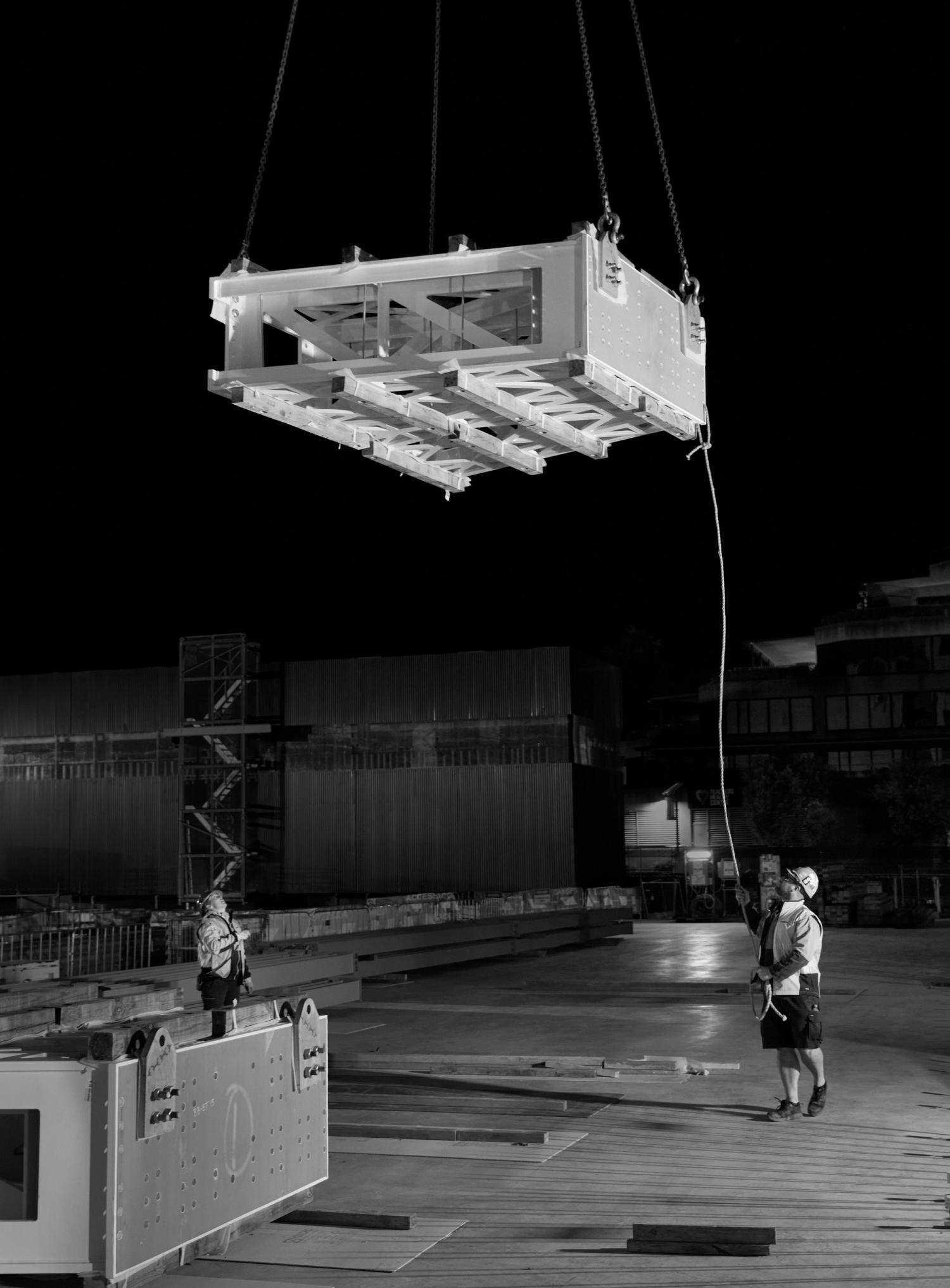 Construction site with large frame being lifted above two small scaled workers