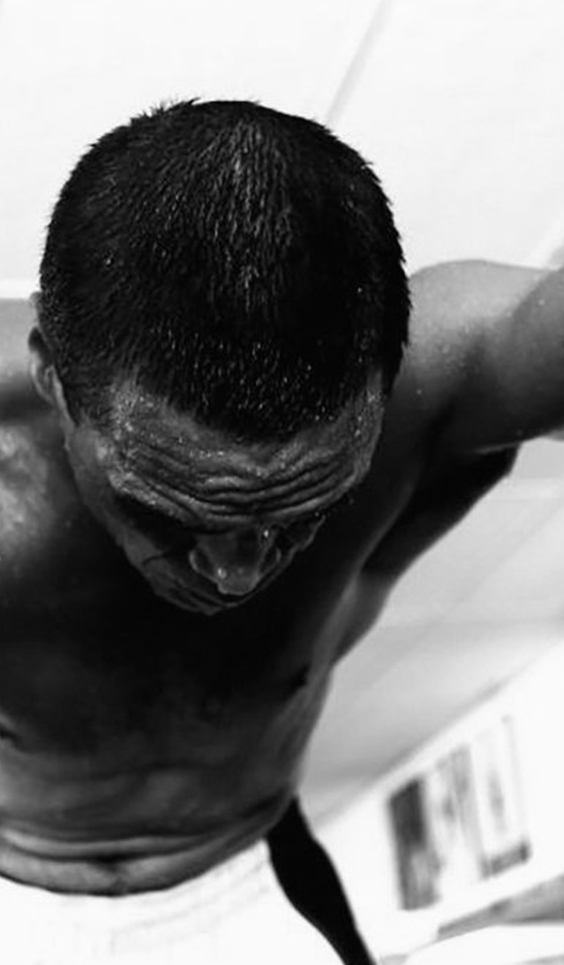 A black and white photograph of a man stretched across the camera, shirtless. His right arm is tattooed and visible.