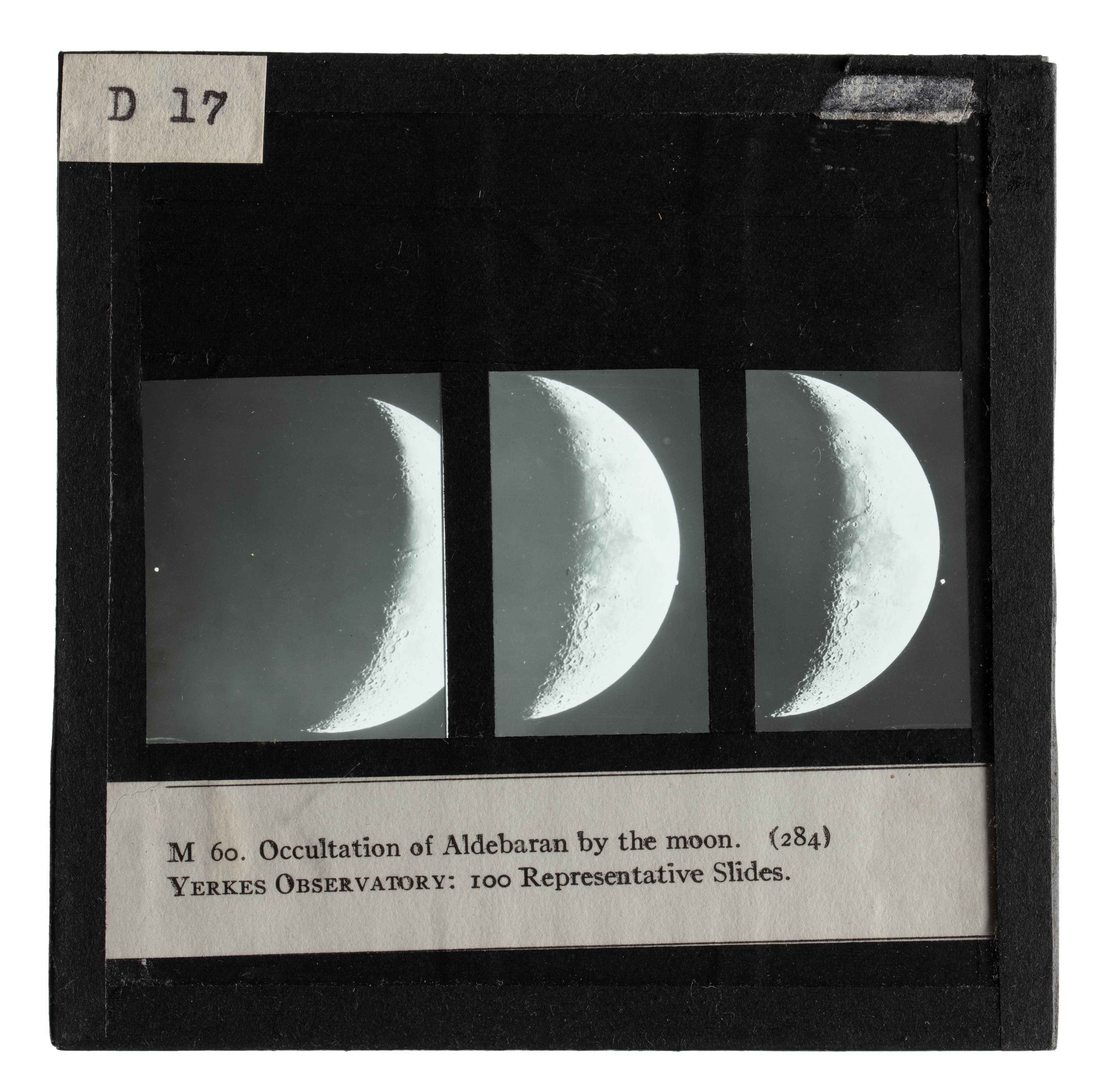 Photograph of a black framed glass plate slide depicting three black and white images of crescent moons. Written on the top of the frame is 'D 17', at the bottom 'M 60. Occulation of Aldebaran by the moon. (284) - YERKES OBSERVATORY: 100 Representative Slides.'.