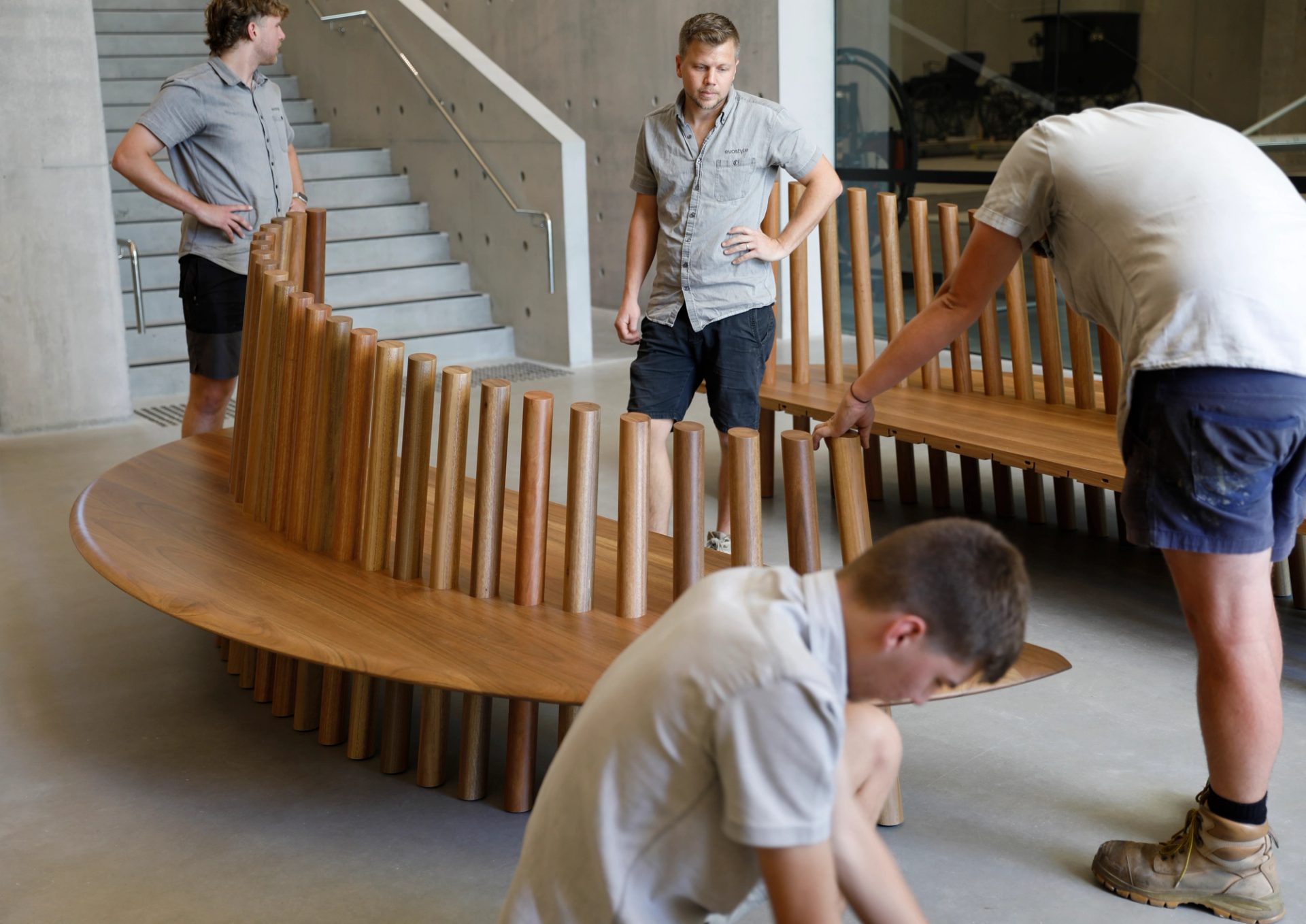 Four men assembling two halves of a large wooden oval shaped seat