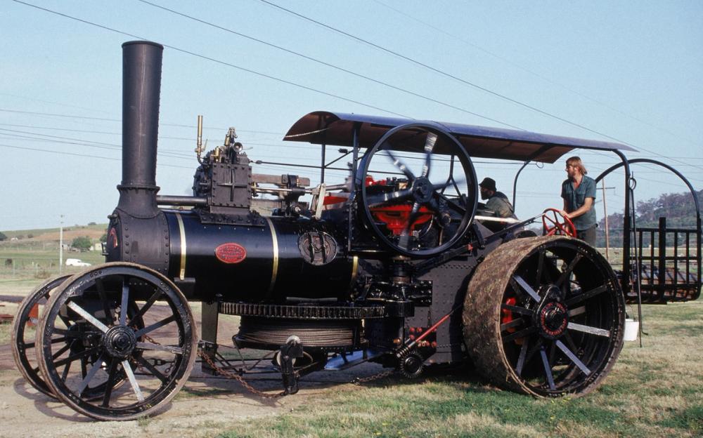 A large steam ploughing engine in a green field with two people on board.