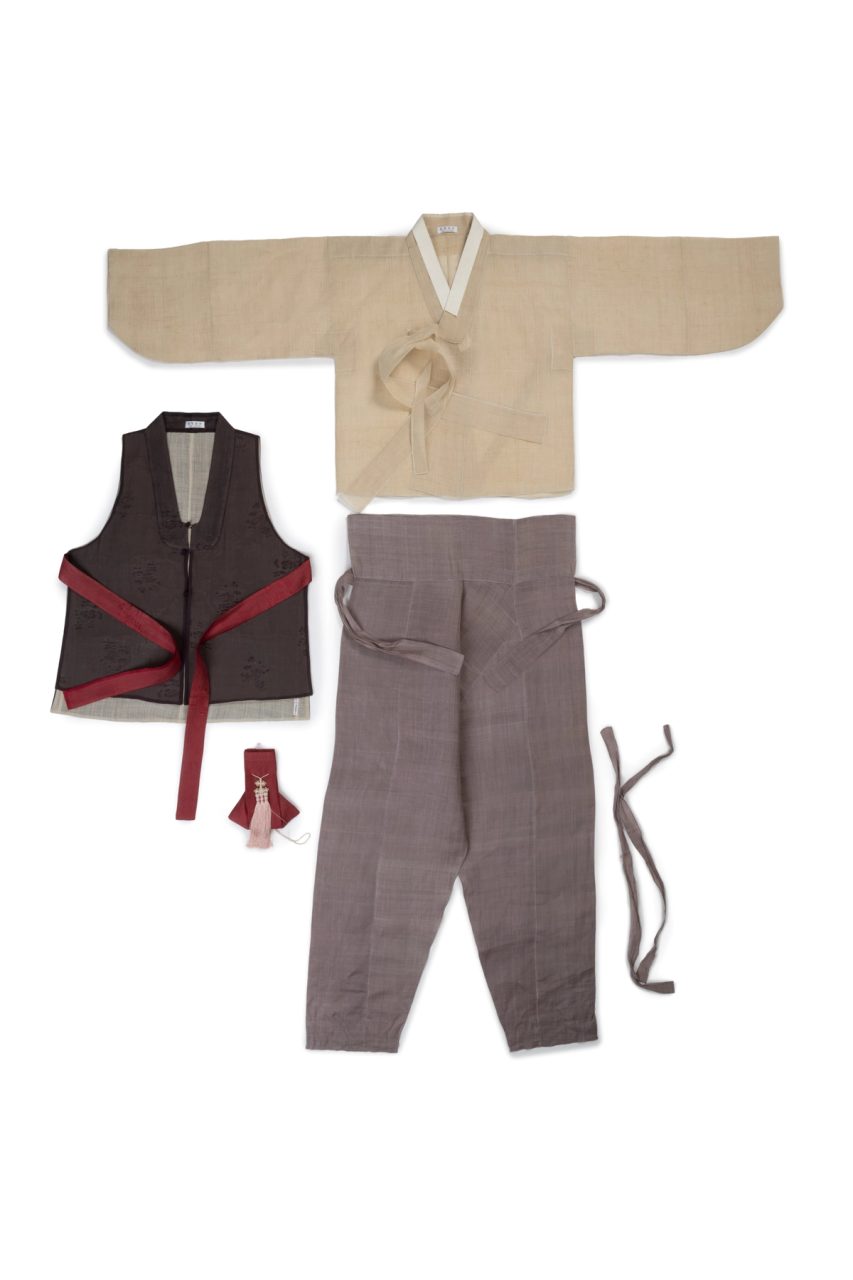 Mens ensemble comprising of a hip length loose fitting jacket of light brown ramie cloth, light purple and brown trousers with ankle ties, short vest made of dark brown self patterned silk gauze with stylised foliate pattern and small purse made of folded maroon self patterned silk gauze over white cotton stiffening.