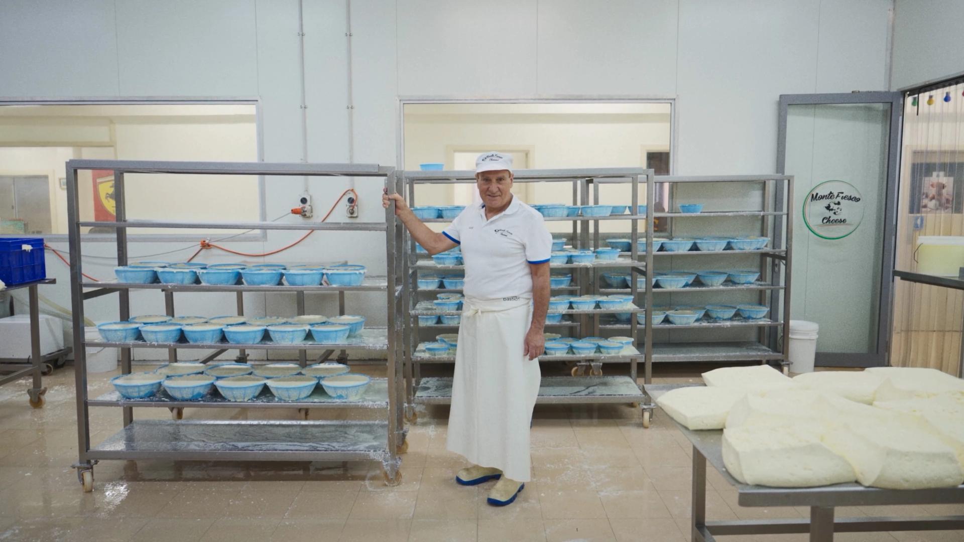 A man standing with a large trolley of cheeses, in a manufacturing factory.
