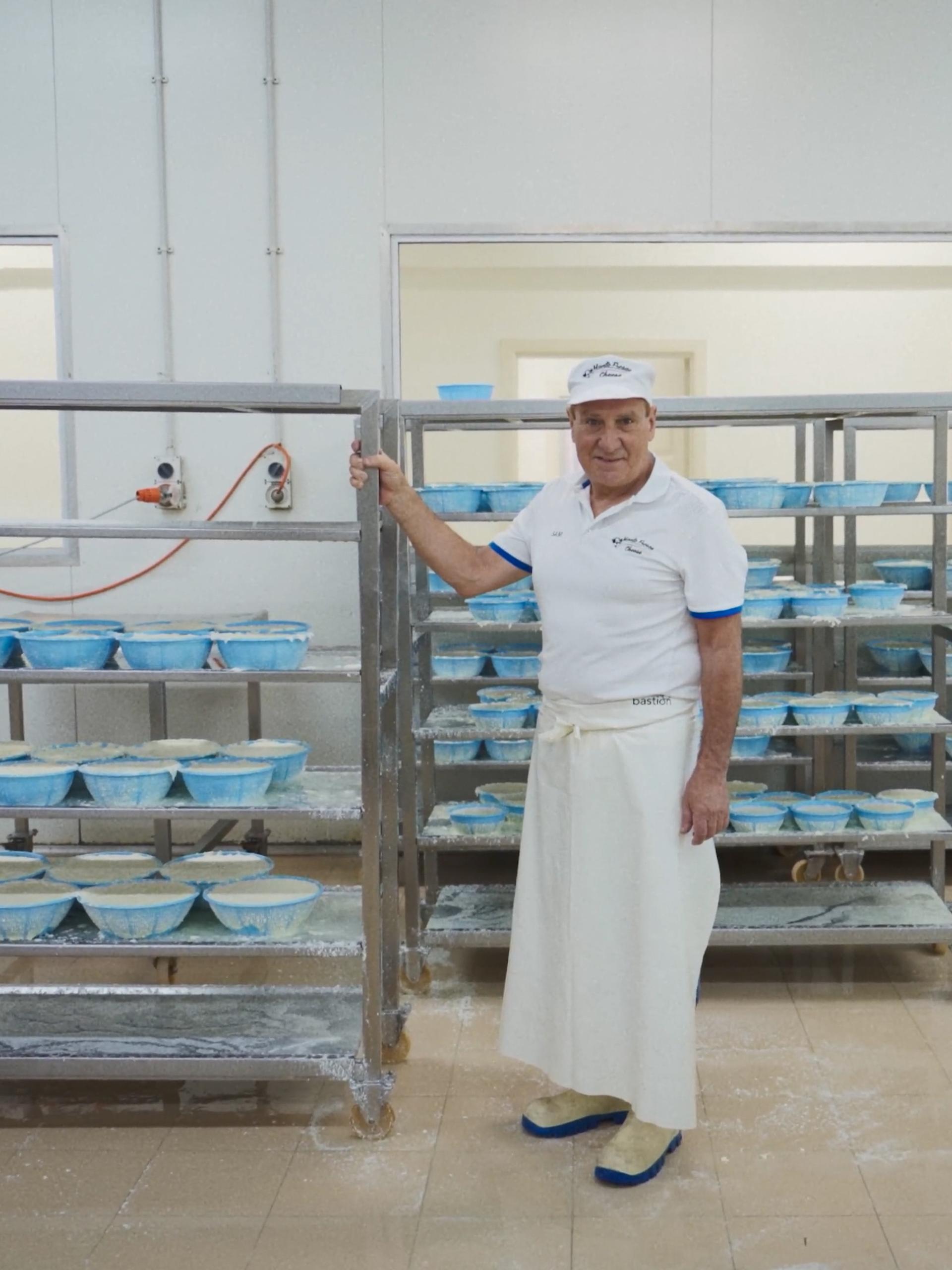 A man standing with a large trolley of cheeses, in a manufacturing factory.