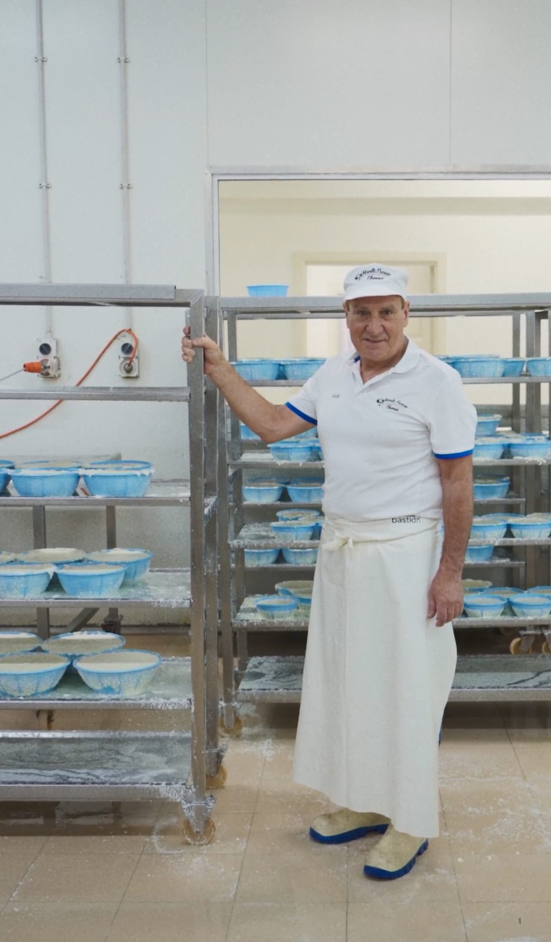 A man standing with a large trolley of cheeses, in a manufacturing factory.