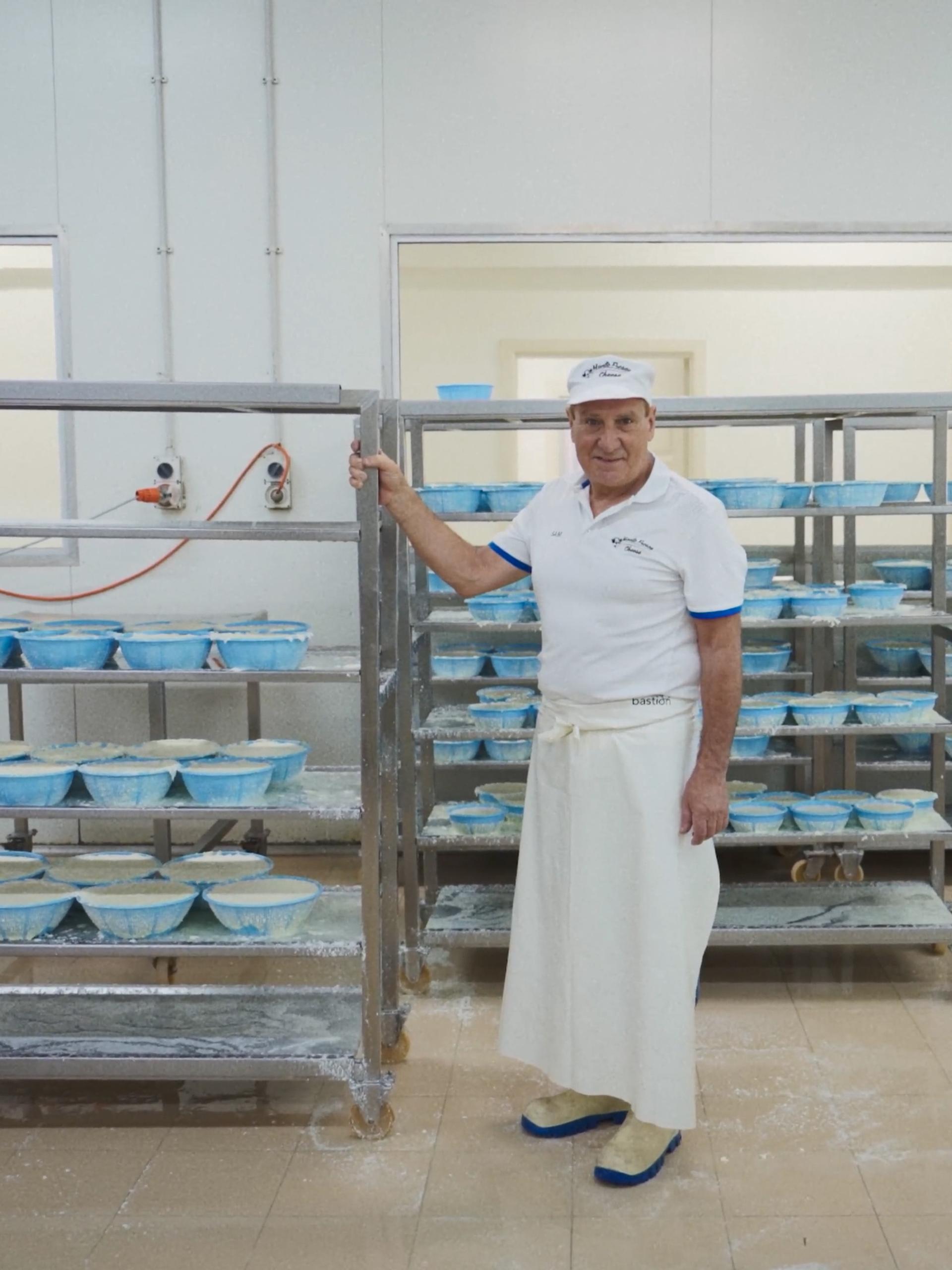 A man standing with a large trolley of cheeses, in a manufacturing factory.