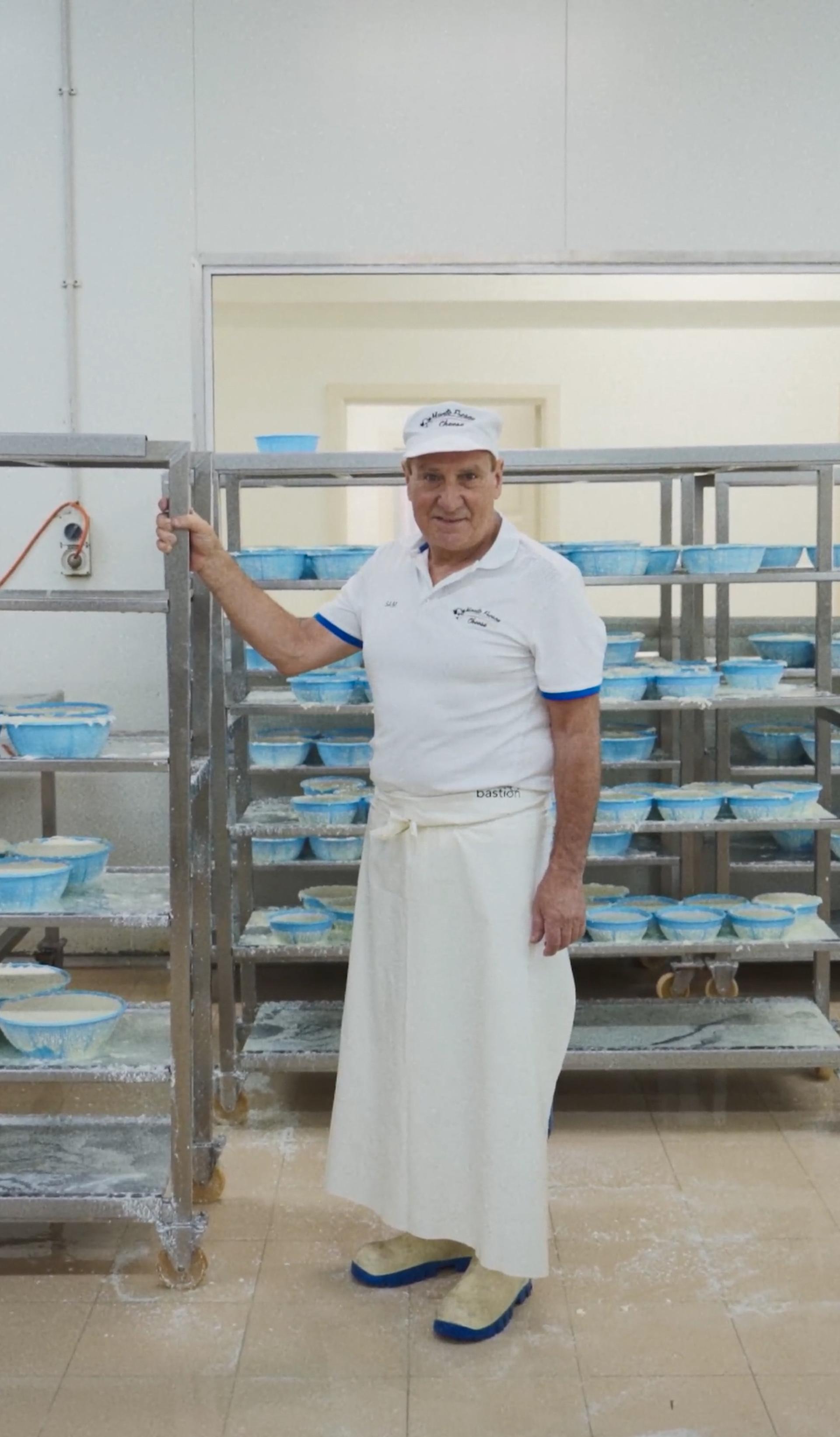 A man standing with a large trolley of cheeses, in a manufacturing factory.