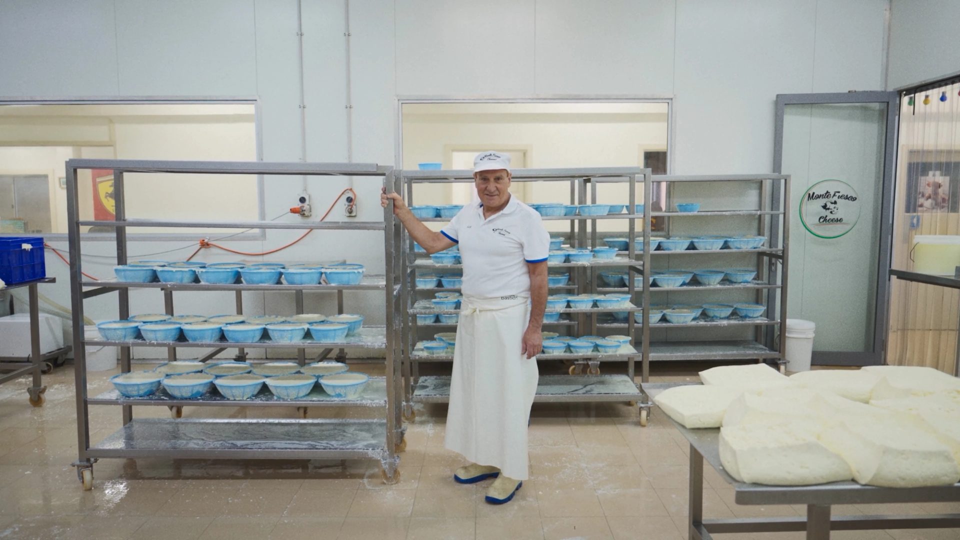 A man standing with a large trolley of cheeses, in a manufacturing factory.