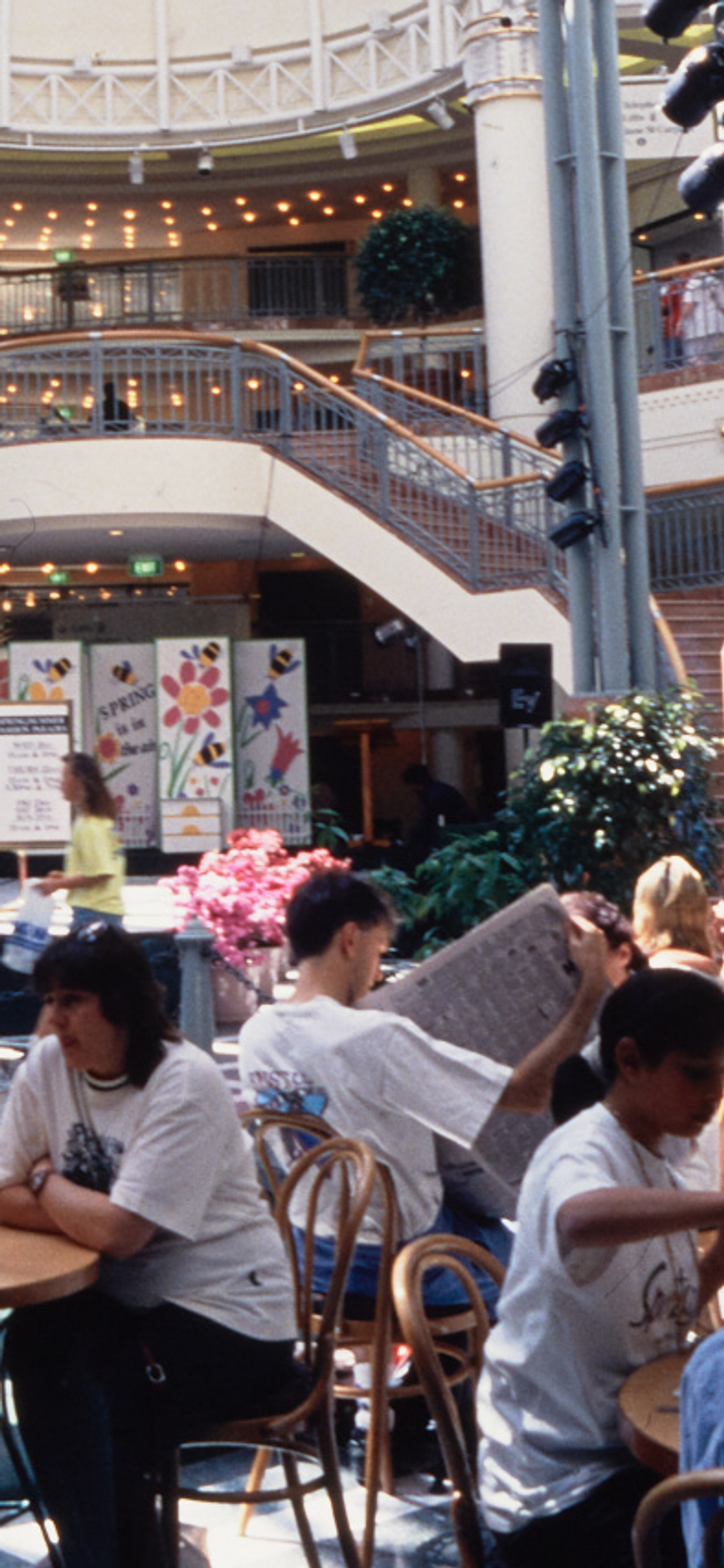 A photograph of the busy Food court at Penrith Plaza, cafe tables filled with guests surround the centre fountain, with a two-way staircase in the background.