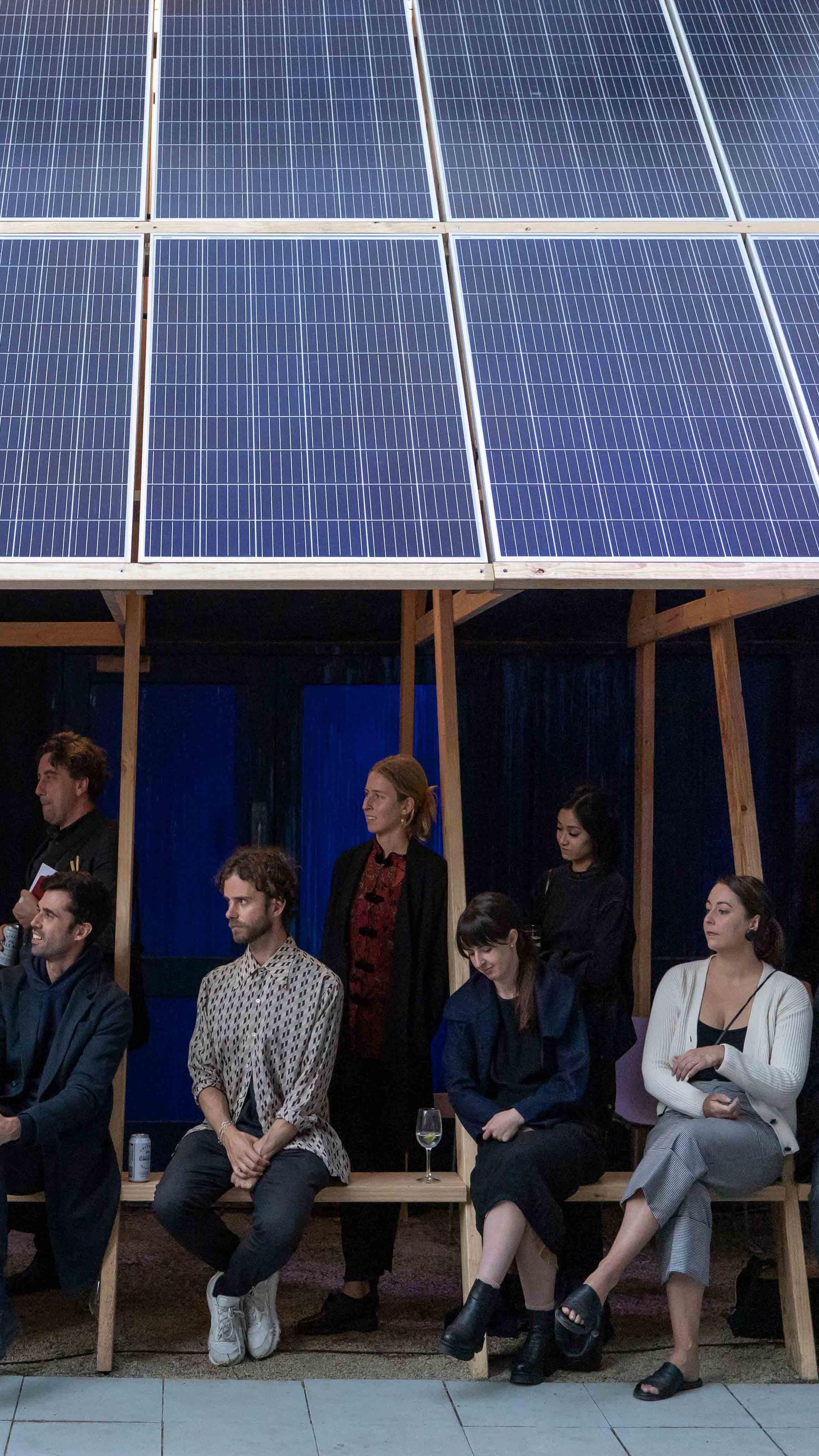 Many people sitting underneath the shelter of solar panels.
