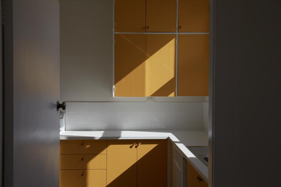 Shadows casting angles across a mustard cabinet-filled kitchen