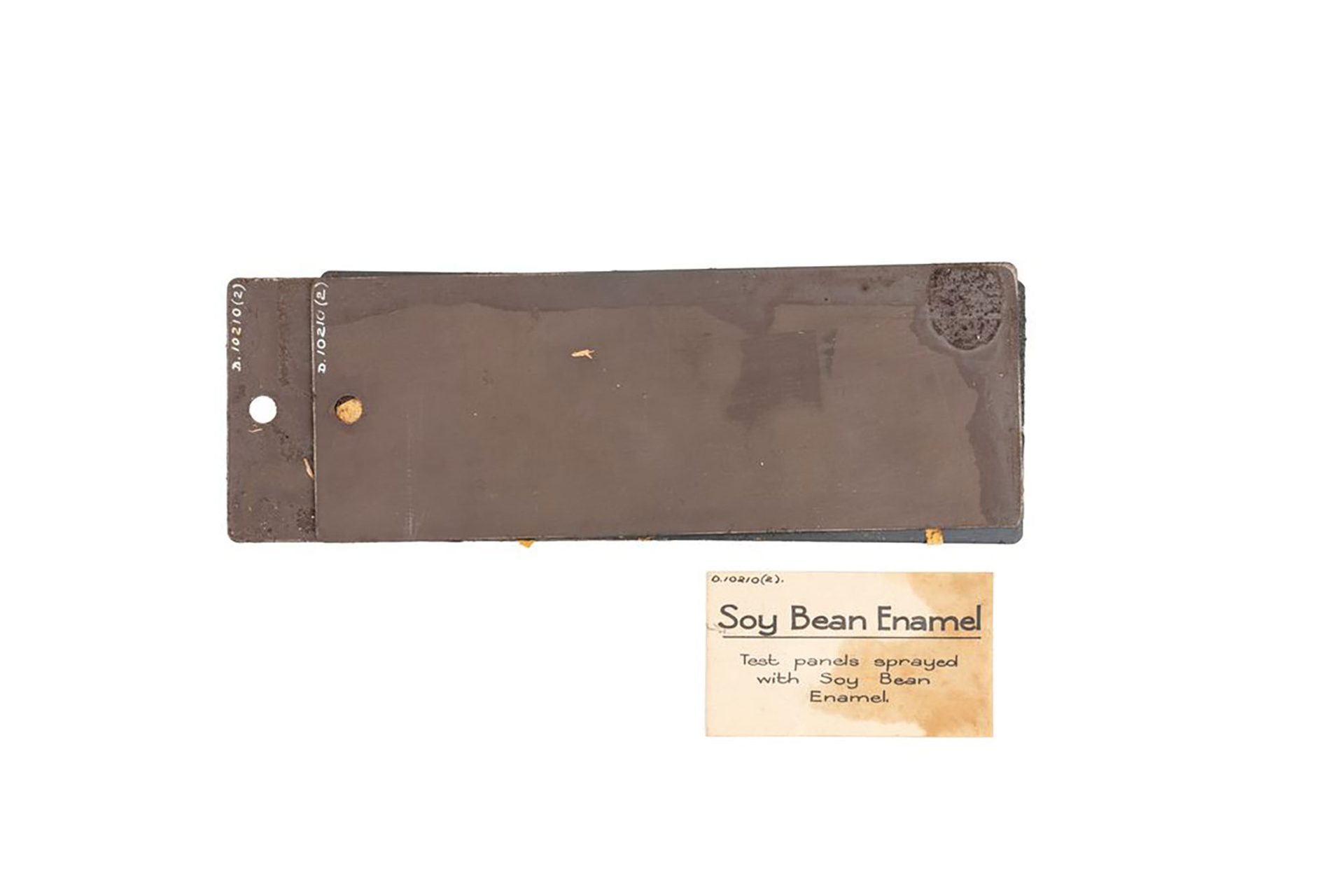 Two rectangular brown specimens of soy bean enamel. There is a museum label that reads ‘Soy bean enamel, test panels sprayed with soy bean enamel.’