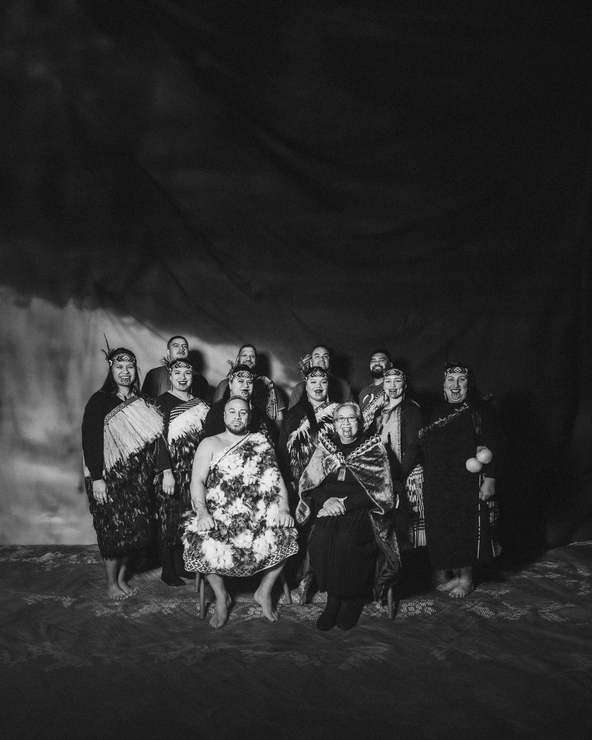A black and white group portrait of the kapa haka group, Te Raranga Whānui. Seated at the front are Laurie Sarich, Neta Sarich. Behind them are Casey Fenton, Moana McLeod, Ashley Simon, Marei Peters, Hope Harris, Tiana Tiakiwai. At the back are Conway McLeod, Rata McGregor Jnr, Josh Simon, Royal Kingi Pita.