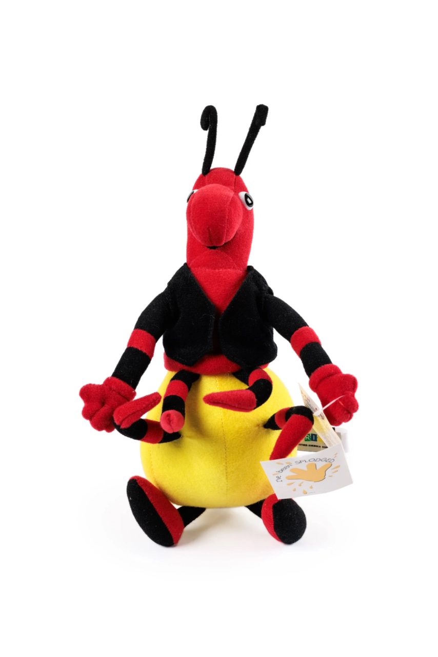 A honey ant soft toy with a yellow rounded lower body, a red upper body and eight red and black striped legs. The ant wears a sleeveless black jacket.