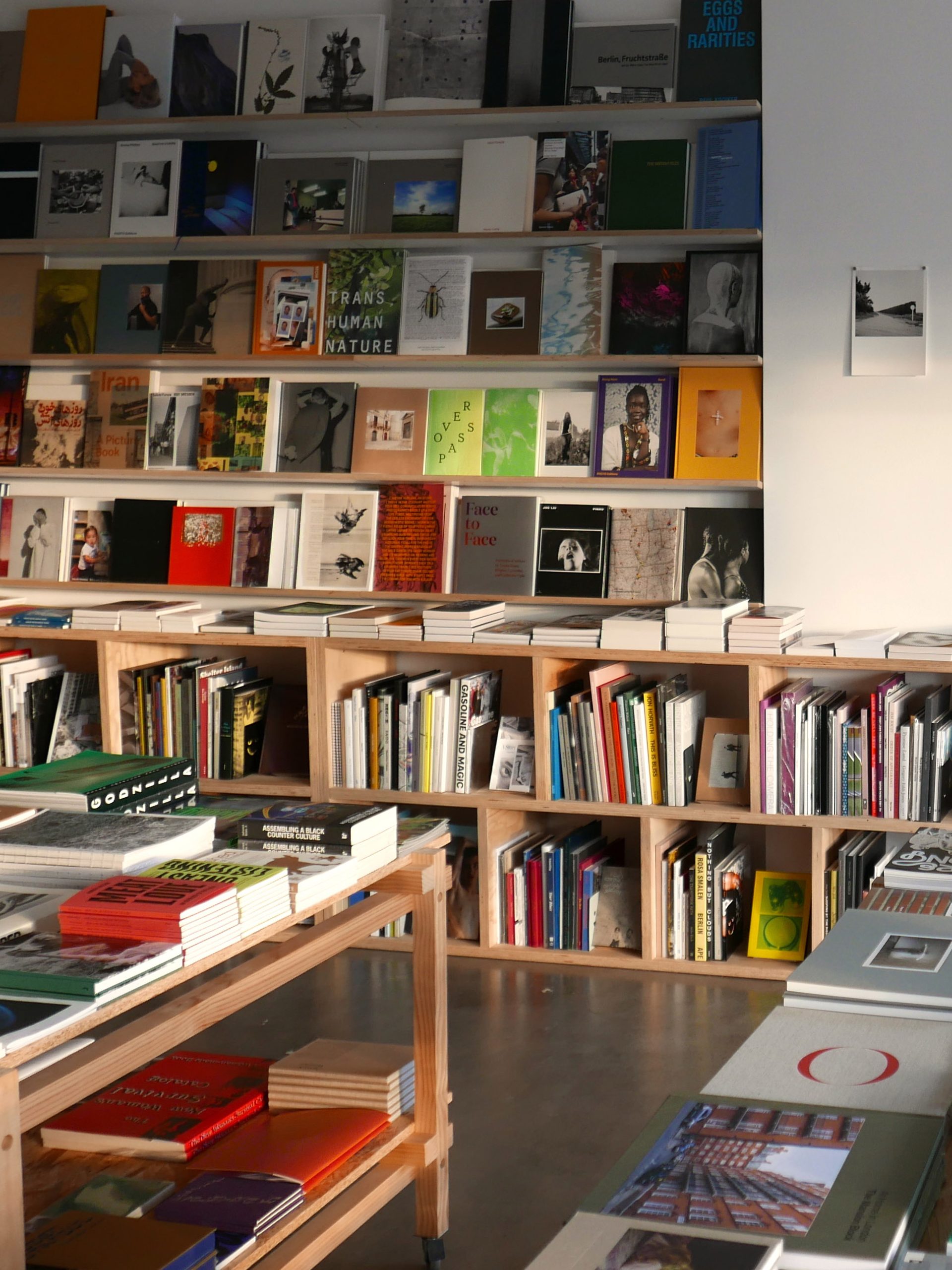 A shop space with polished concrete floors and white walls. Colourful books sit on wooden shelves and ta