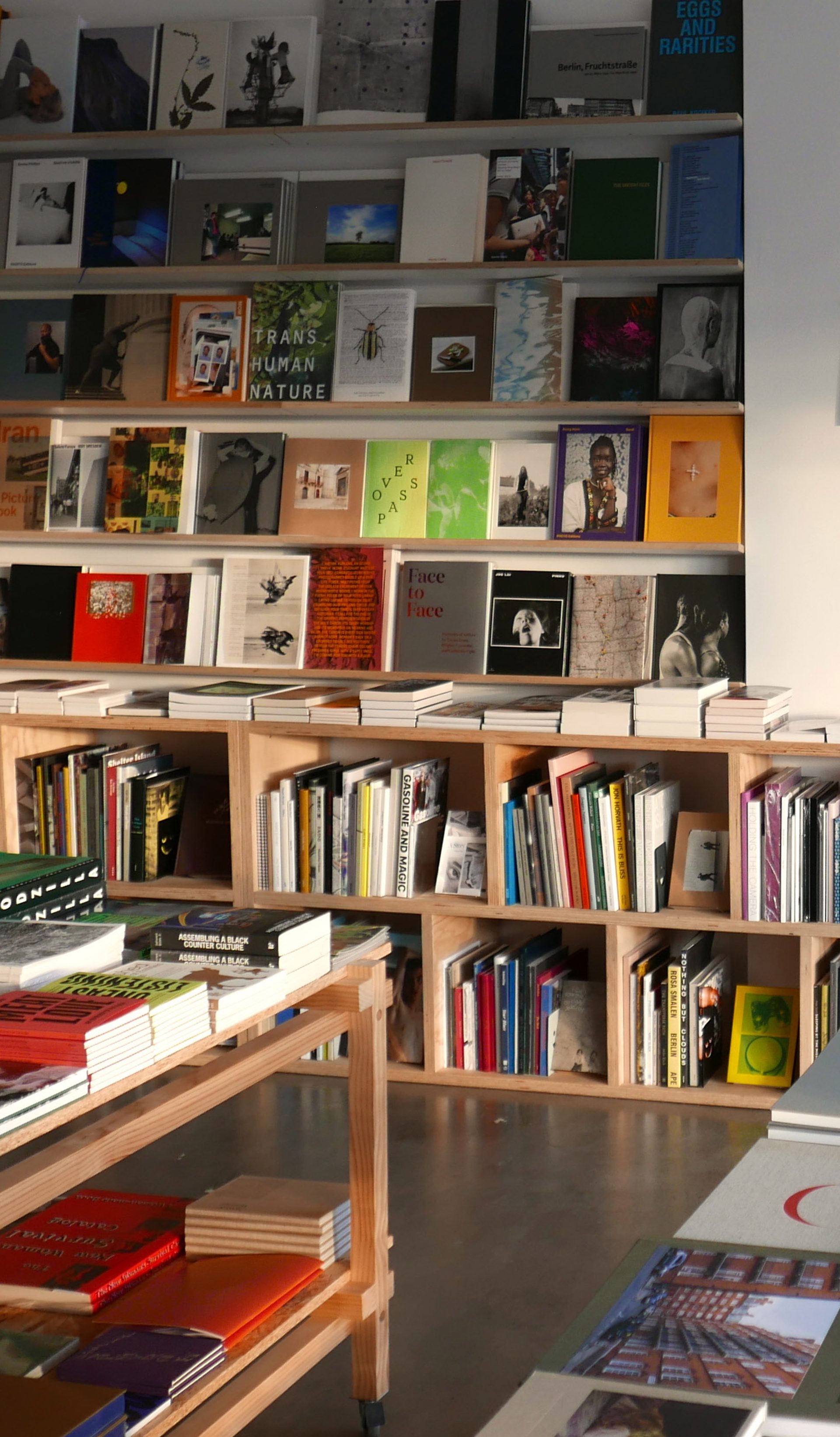 A shop space with polished concrete floors and white walls. Colourful books sit on wooden shelves and ta