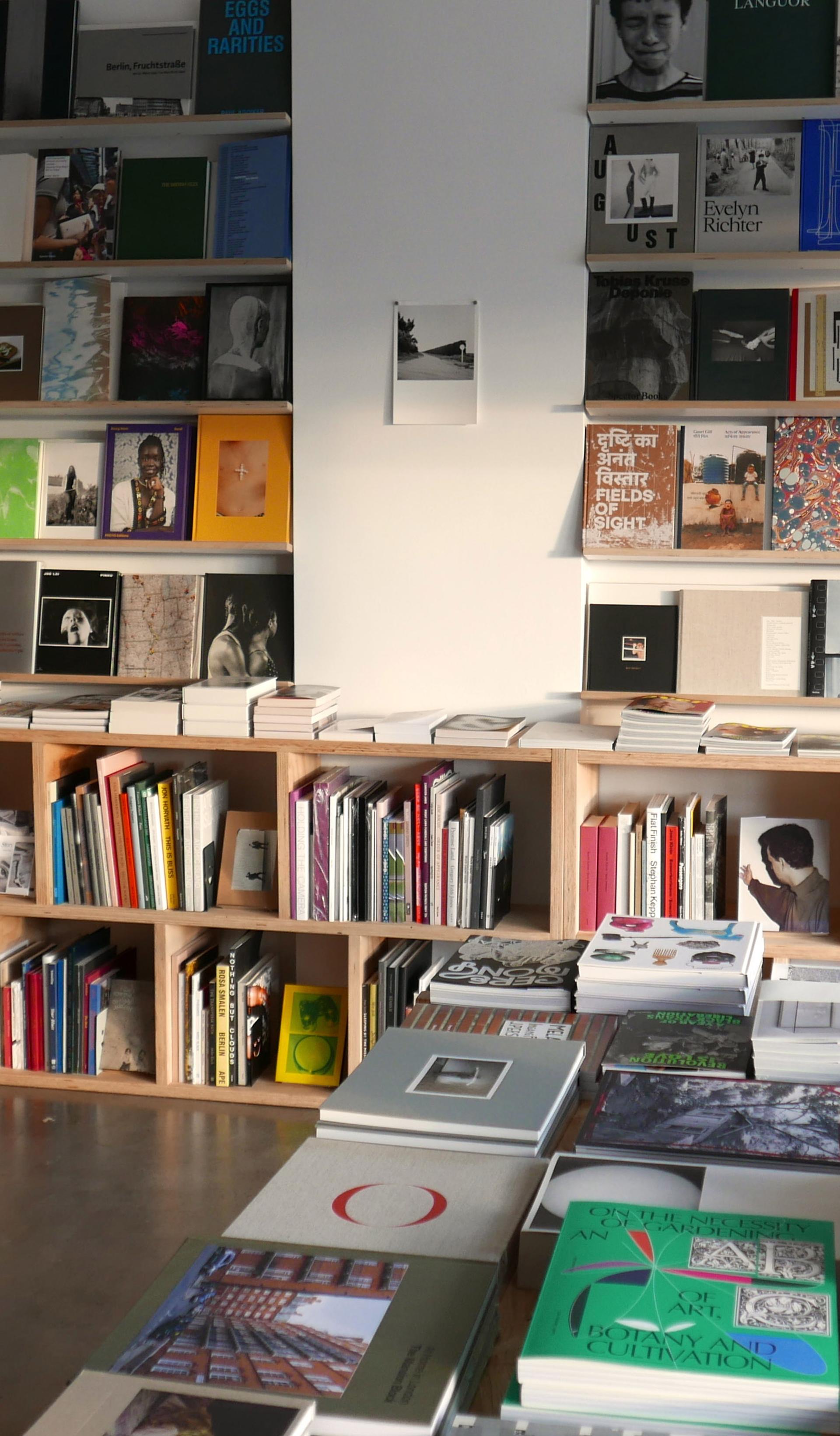 A shop space with polished concrete floors and white walls. Colourful books sit on wooden shelves and ta