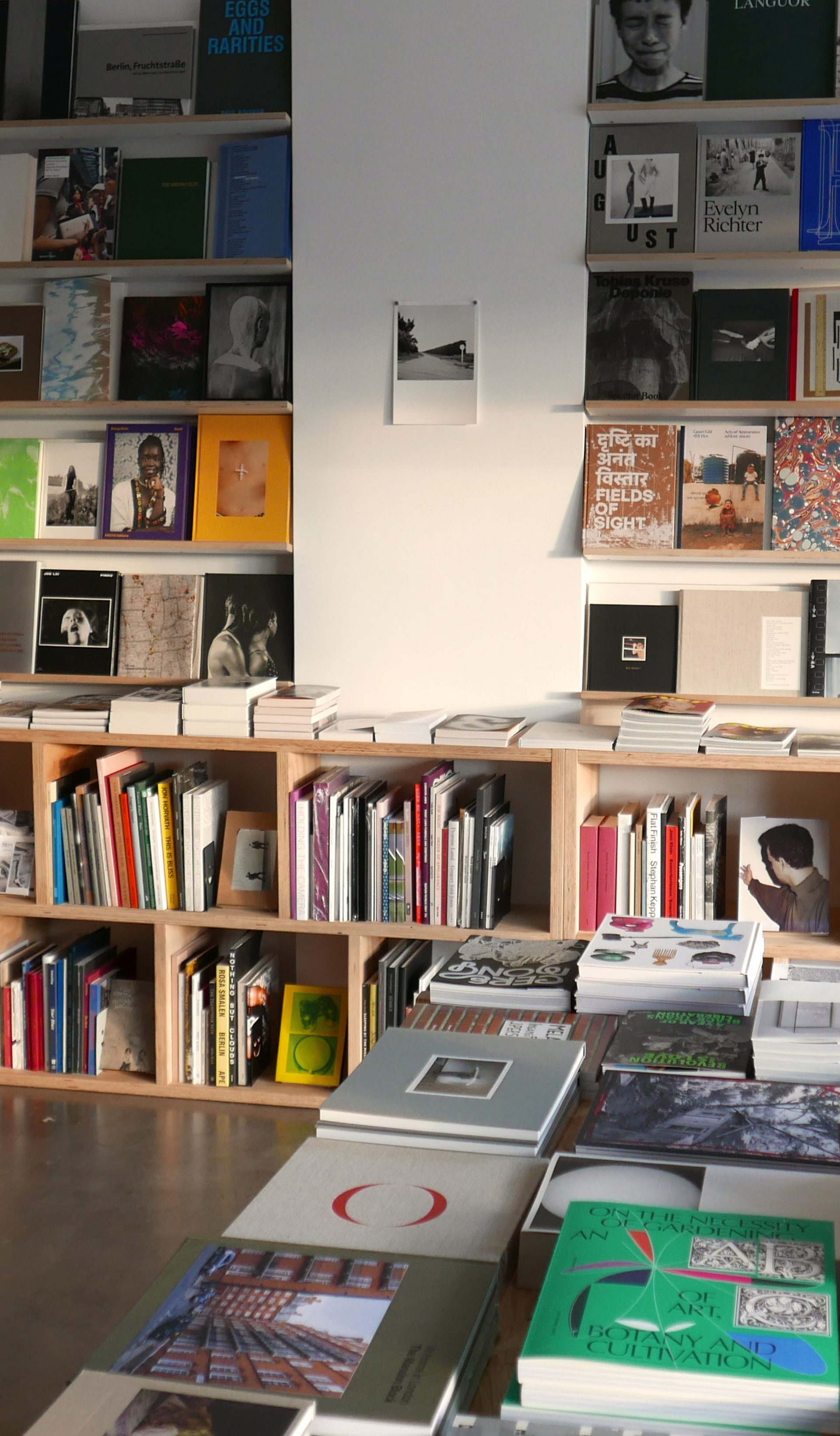 A shop space with polished concrete floors and white walls. Colourful books sit on wooden shelves and ta